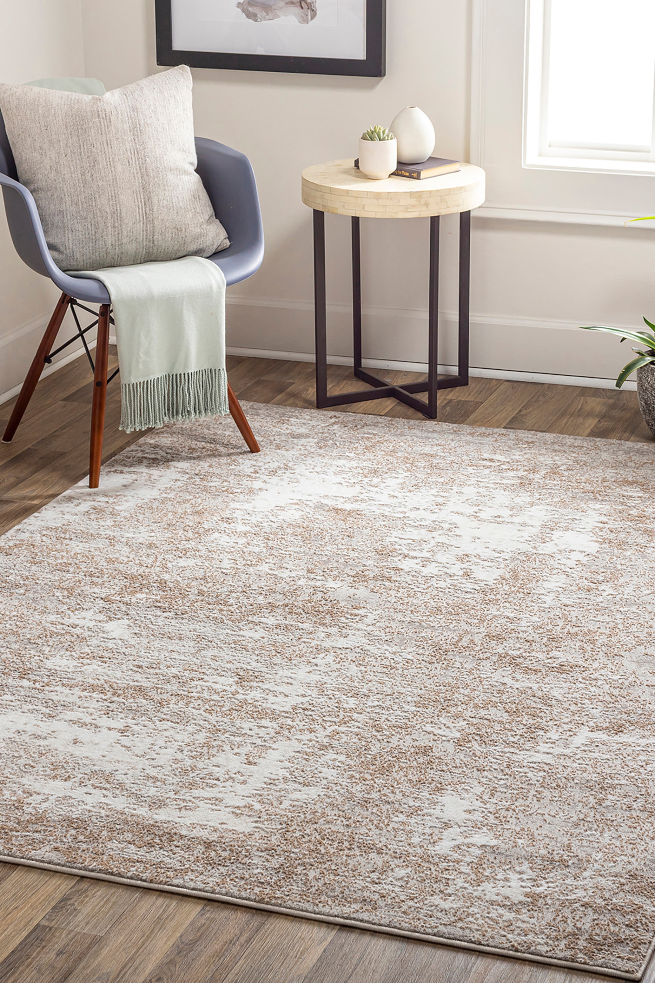 View larger image: An area rug featuring an abstract, distressed pattern in shades of beige and off-white is lying on a wooden floor. The rug is showcasing a textured, mottled design with a low pile and a clean, bound edge.