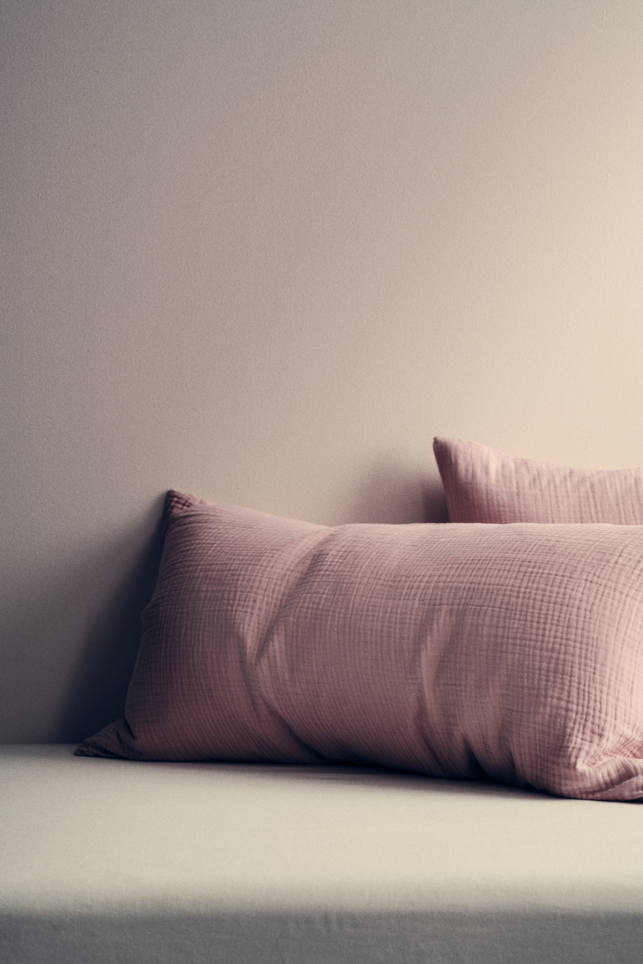 Größeres Bild anzeigen: Zwei rosa Kissen liegen horizontal und präsentieren eine markante, geknitterte Gaze-Textur. Das größere Kissen befindet sich im Vordergrund, während ein zweites Kissen teilweise dahinter erscheint.