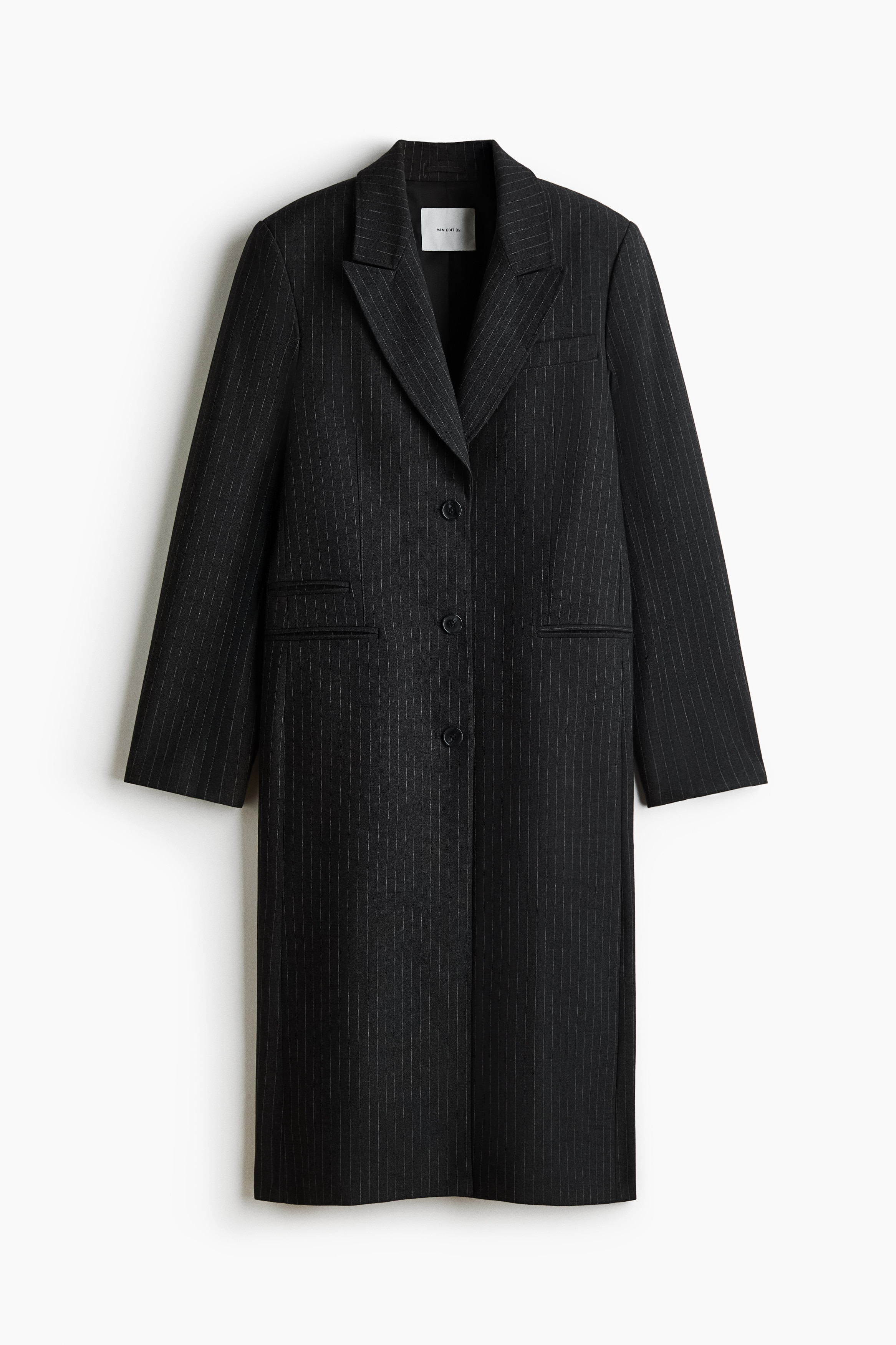 A modelo veste um blazer de trespasse simples em cinzento escuro Ã s riscas finas sobre uma camisola preta de gola alta. O blazer oversized apresenta lapelas em bico, fecho frontal com botÃµes e ombros estruturados, e Ã© complementado por uma mala grande preta segurada Ã  frente.