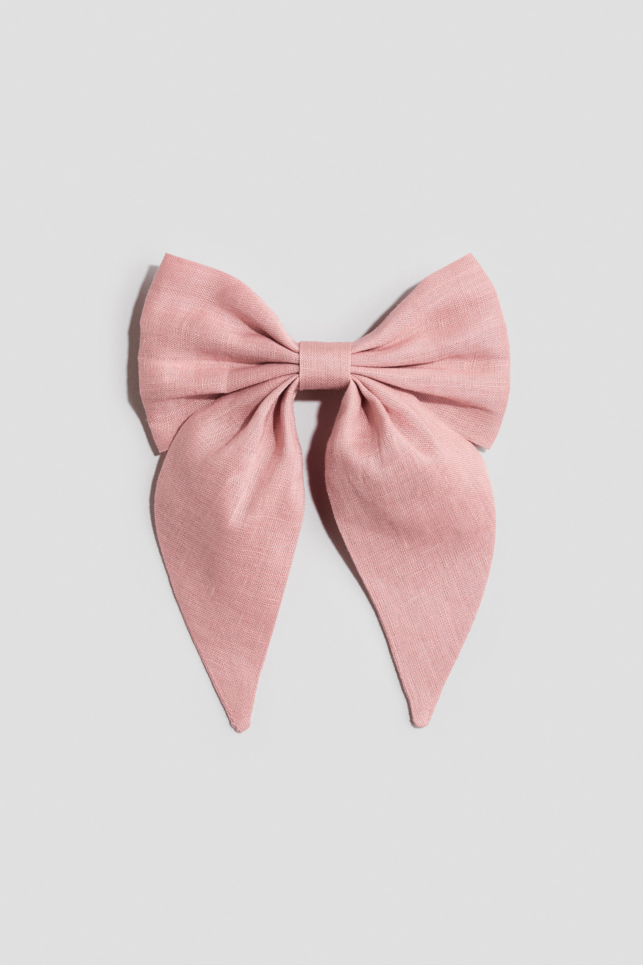 View larger image: A large bow, part of a metal hair clip, is showcased front-facing in a soft pink linen. It features a gathered center and two long, pointed tails extending downward.