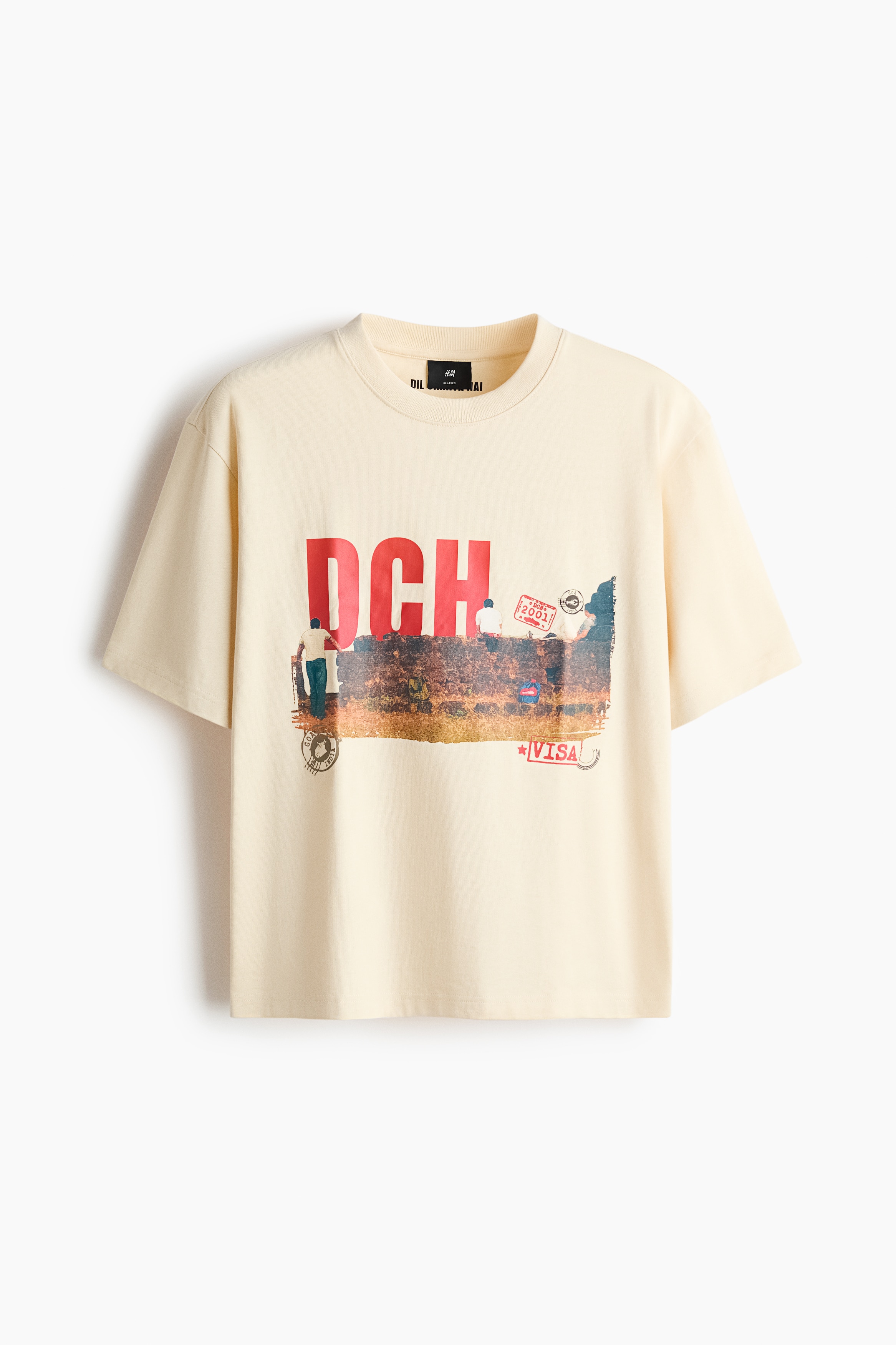 The model is wearing a cream-coloured T-shirt in heavyweight cotton jersey, paired with dark blue jeans. The relaxed-fit tee features dropped shoulders, a ribbed crew neck, and a large front graphic print with the red letters "DCH" and stamp motifs.