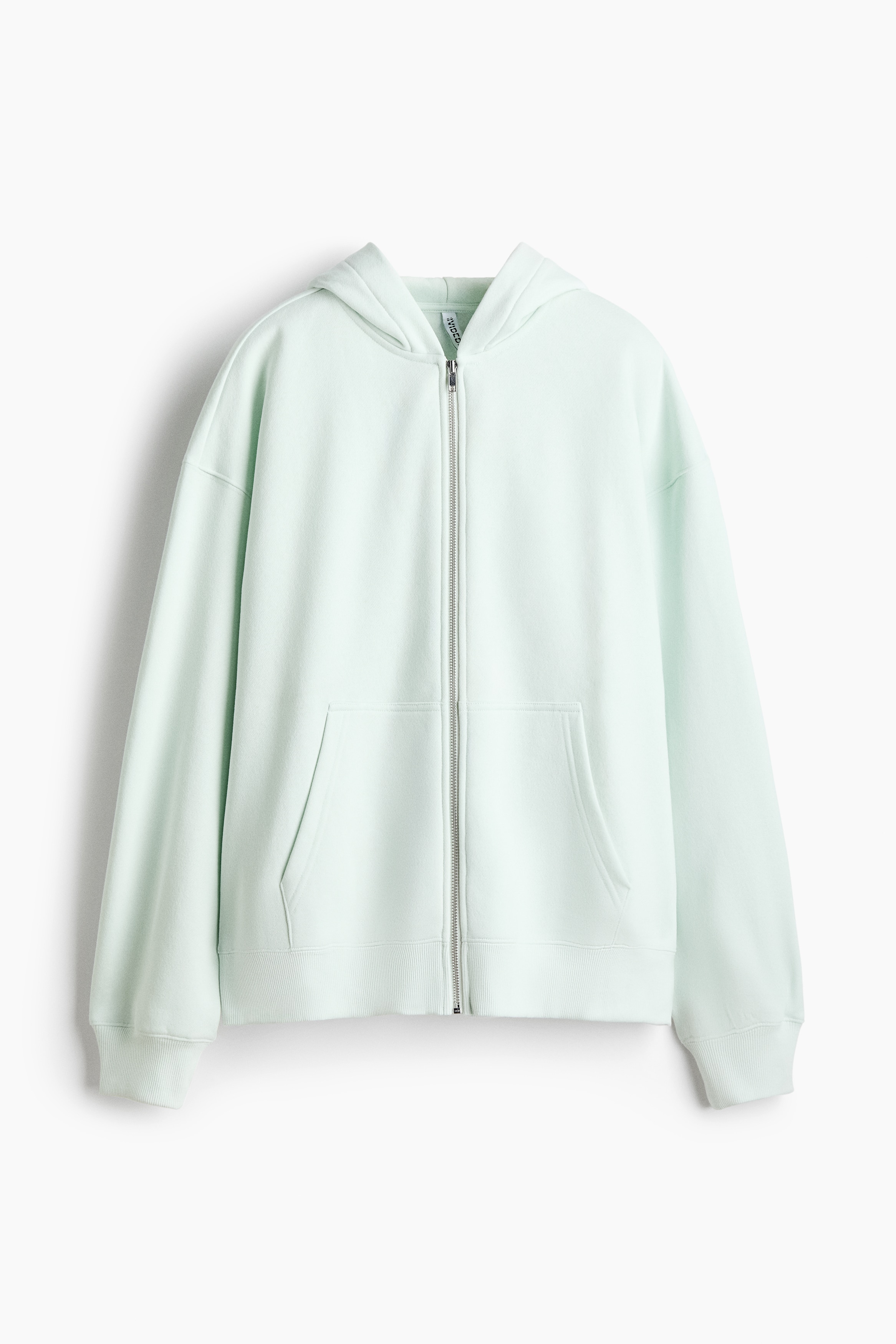 A light mint green zip-up hoodie is worn in a front-facing view, featuring an oversized fit with dropped shoulders, a hood worn over the head, and ribbed cuffs and hem. The hoodie is styled partially unzipped at the top and bottom, showing front pockets and a striped shirt collar underneath.