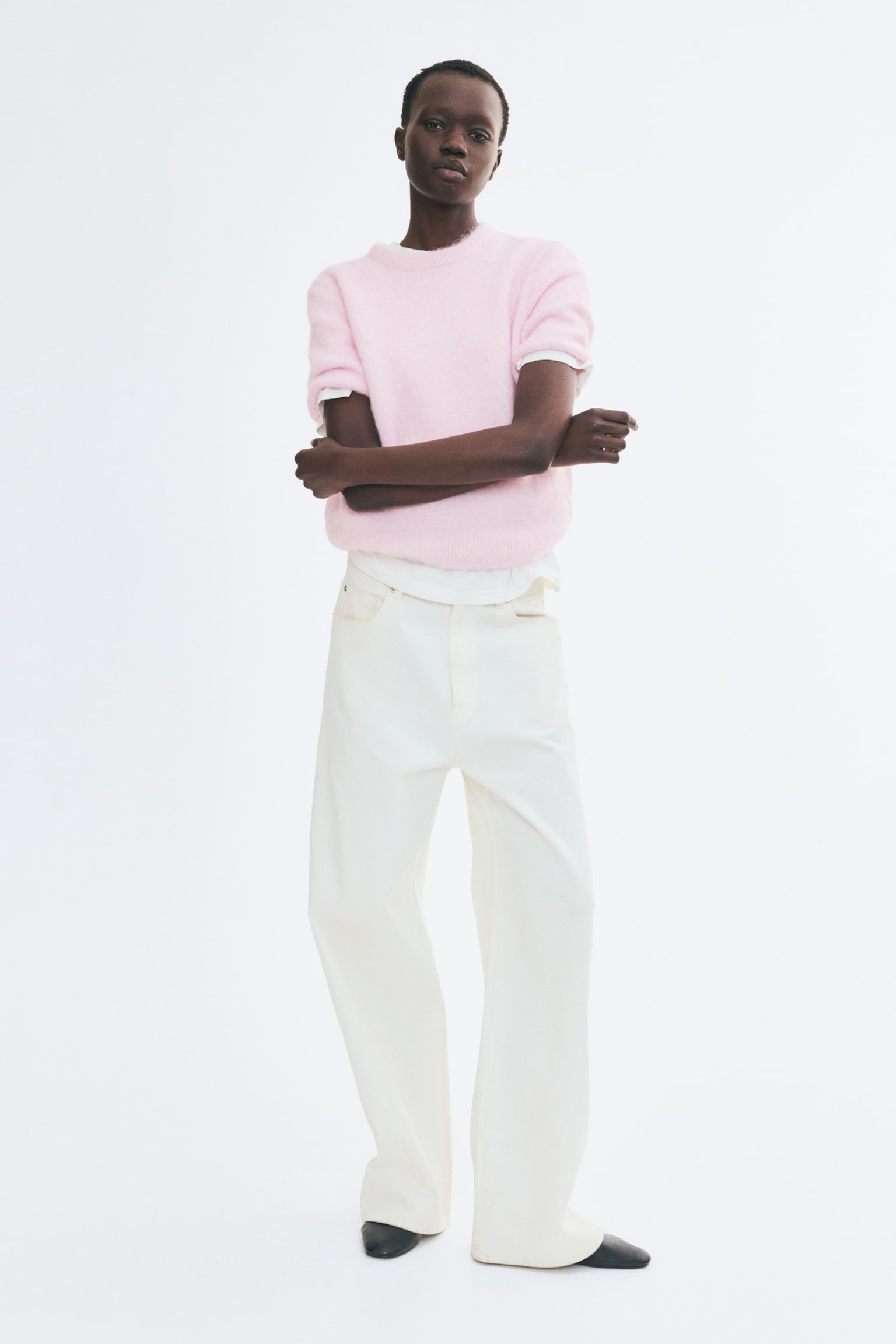 A pink fluffy jumper is laid flat, showcasing a crew neck, short sleeves with ribbed cuffs, and a ribbed hem. A light-coloured tag is visible at the back of the neck. - 1