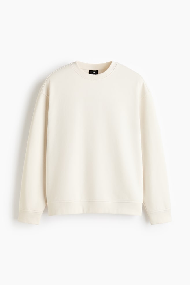 Una felpa color crema mostra la sua vista frontale, caratterizzata da un girocollo, polsini a coste, un orlo a coste e un'etichetta nera H&M visibile sul retro del collo. - 1