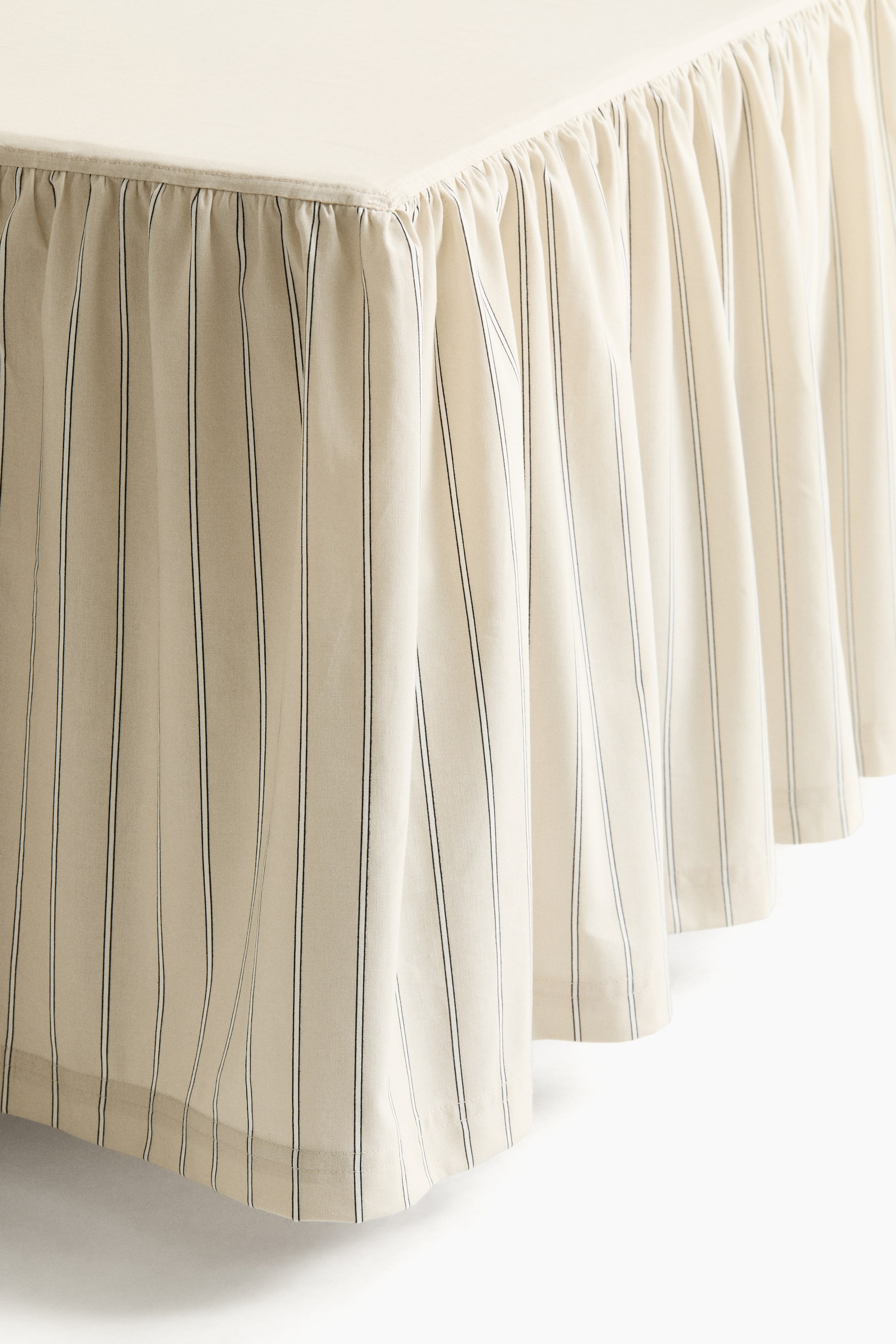 View larger image: A flounced valance covers a rectangular surface, viewed from a corner. It showcases a softly draping cream-coloured fabric with thin, vertical black stripes, forming gentle gathers and pleats.