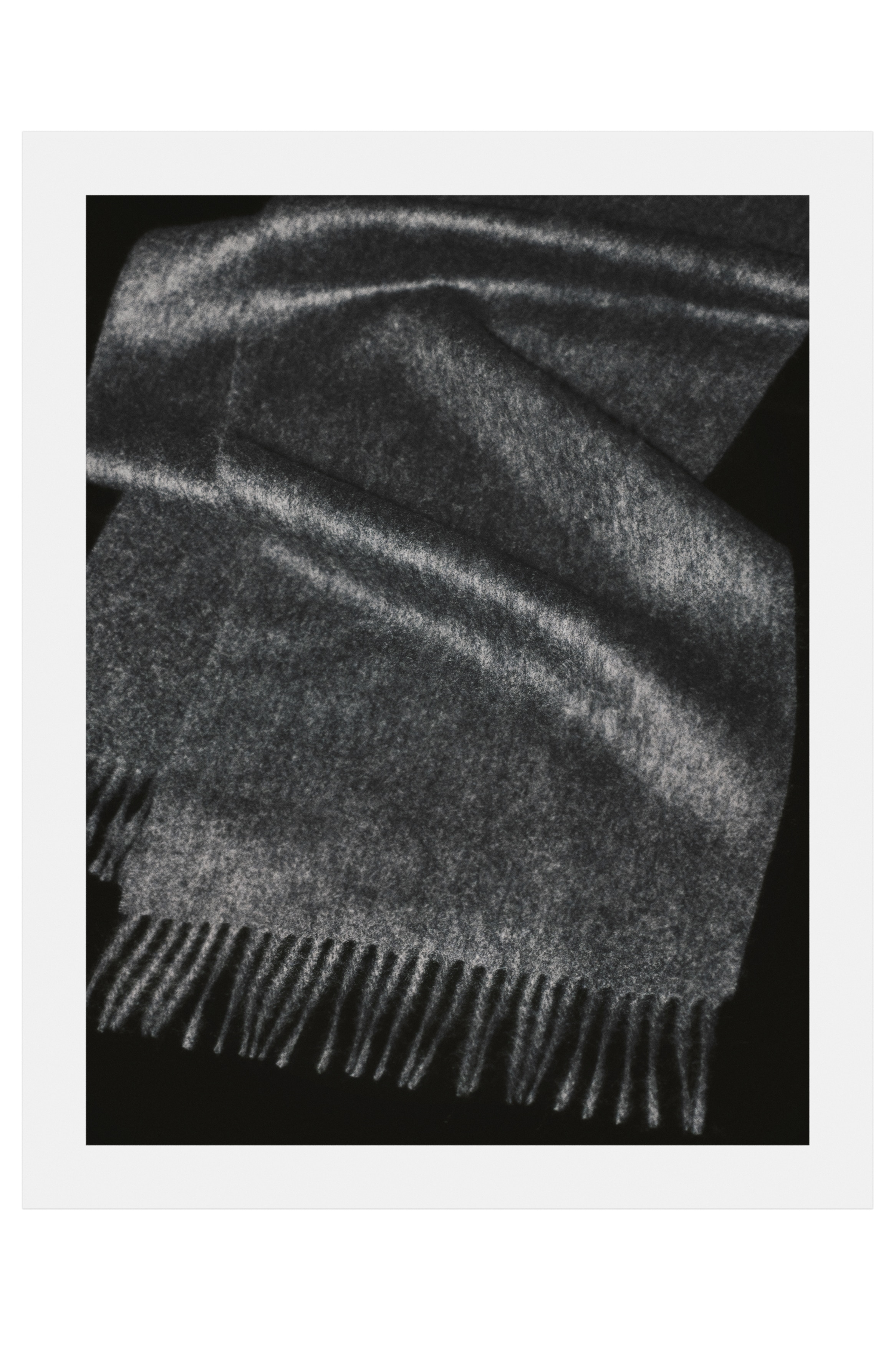 Una sciarpa in cashmere grigio scuro Ã¨ posizionata frontalmente, distesa in piano per mostrare la sua morbida texture spazzolata. La sciarpa presenta dettagli con frange intrecciate lungo il bordo inferiore visibile.