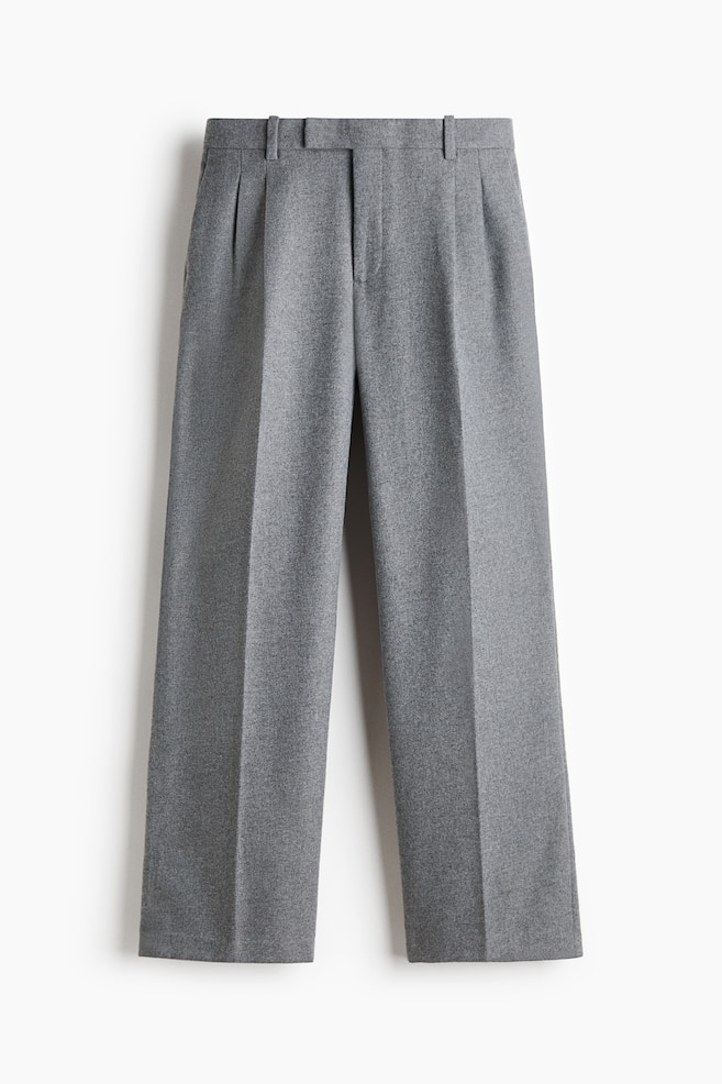Le pantalon gris est présenté de face, avec une ceinture structurée à passants et une fermeture frontale dissimulée. Le modèle met en valeur un pli simple sur le devant et des plis marqués au fer, descendant au centre des jambes droites et larges. - 1
