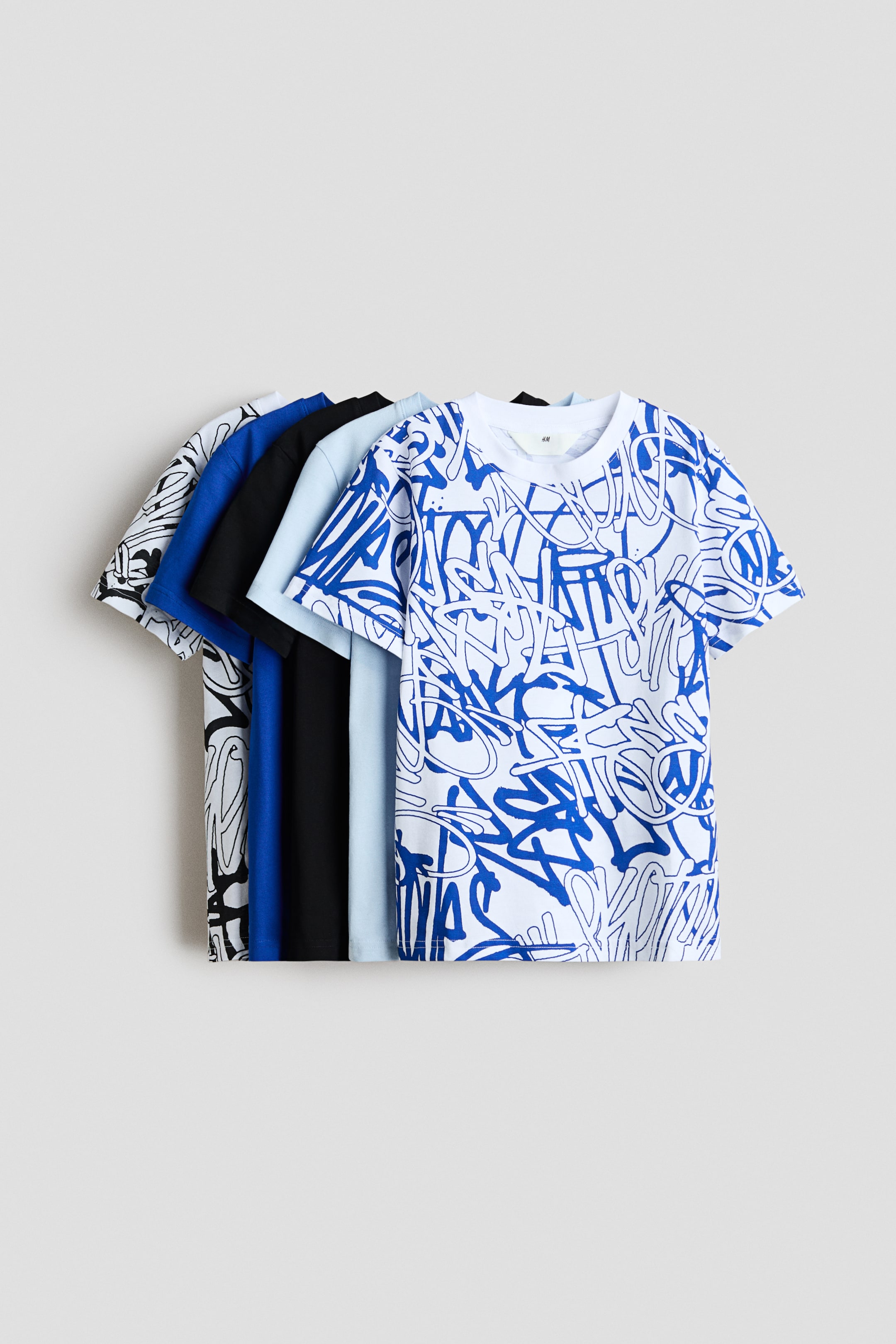 View larger image: T-shirts crafted from soft cotton jersey are displayed with their fronts fanned out from left to right. They showcase a variety of designs, including solid light blue, black, royal blue, and white adorned with graffiti-style prints in blue or black. Each T-shirt features a round, rib-trimmed neckline.