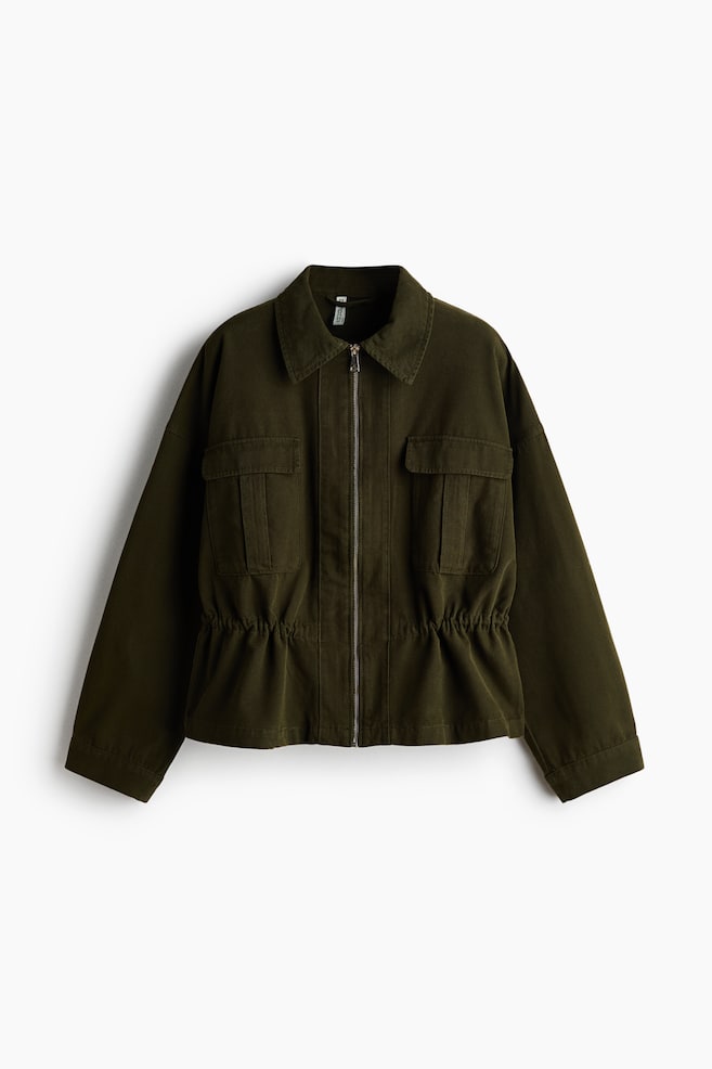 The olive green jacket is featuring a full-zip front closure, a pointed collar, two chest flap pockets, and a cinched waist, presented facing straight on. - 1