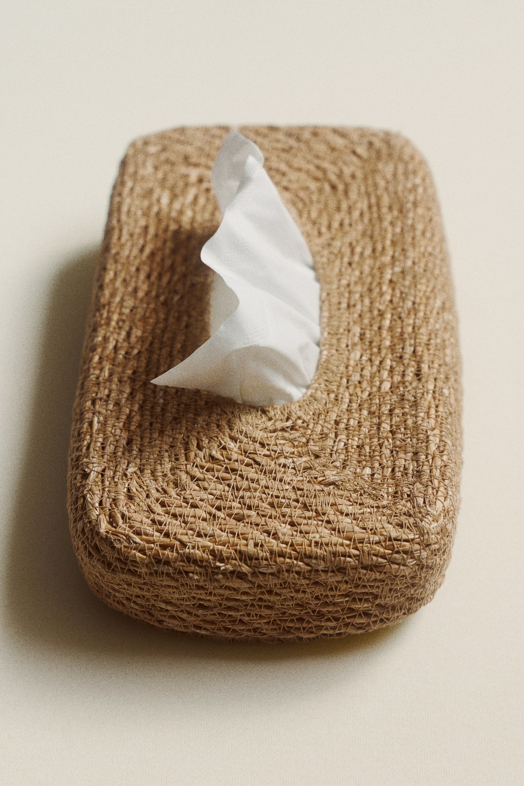 Visualizza immagine più grande: Una copertura rettangolare per scatole di fazzoletti, intrecciata con fibre naturali di colore marrone chiaro, è vista da un'angolazione leggermente dall'alto, con un fazzoletto bianco che emerge dalla sua apertura ovale superiore.