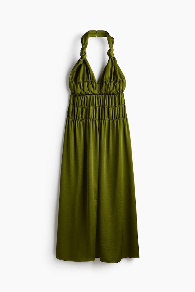 An olive green halter neck maxi dress is hanging frontally, featuring twisted straps knotting at the neck, a gathered V-neckline, and a smocked elasticated waist. Its long skirt is flowing down from the waist. - 1