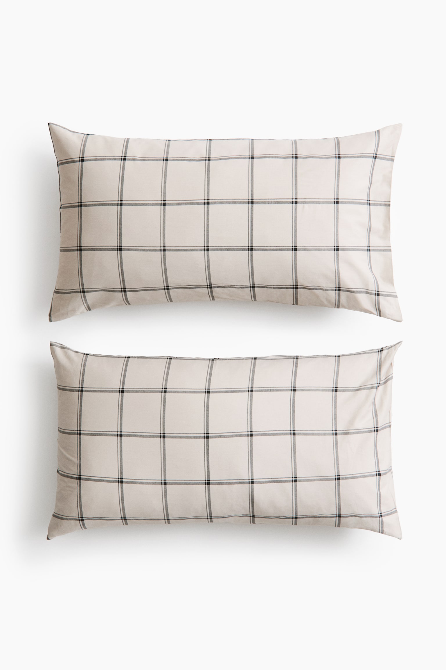 Two rectangular pillowcases in light beige cotton sateen are lying flat, front-facing, in a vertical stack. They display a clean, dark grey and black grid pattern across the smooth, subtly sheened fabric.