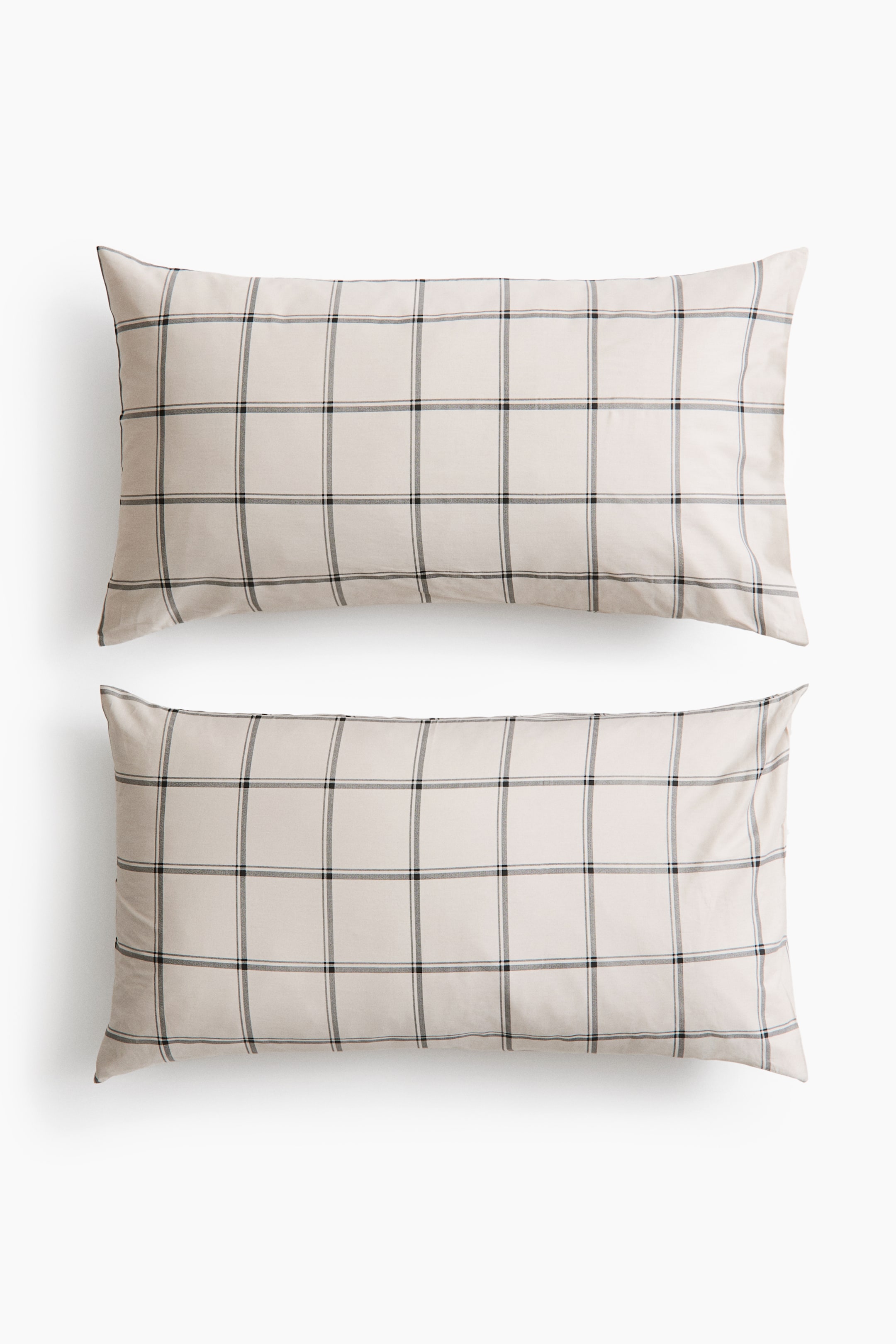 View larger image: Two rectangular pillowcases in light beige cotton sateen are lying flat, facing front in a vertical stack. They display a clean, dark grey and black grid pattern across the smooth, subtly sheened fabric.