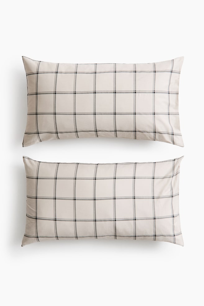 Two rectangular pillowcases in light beige cotton sateen are lying flat, facing front in a vertical stack. They display a clean, dark grey and black grid pattern across the smooth, subtly sheened fabric. - 1