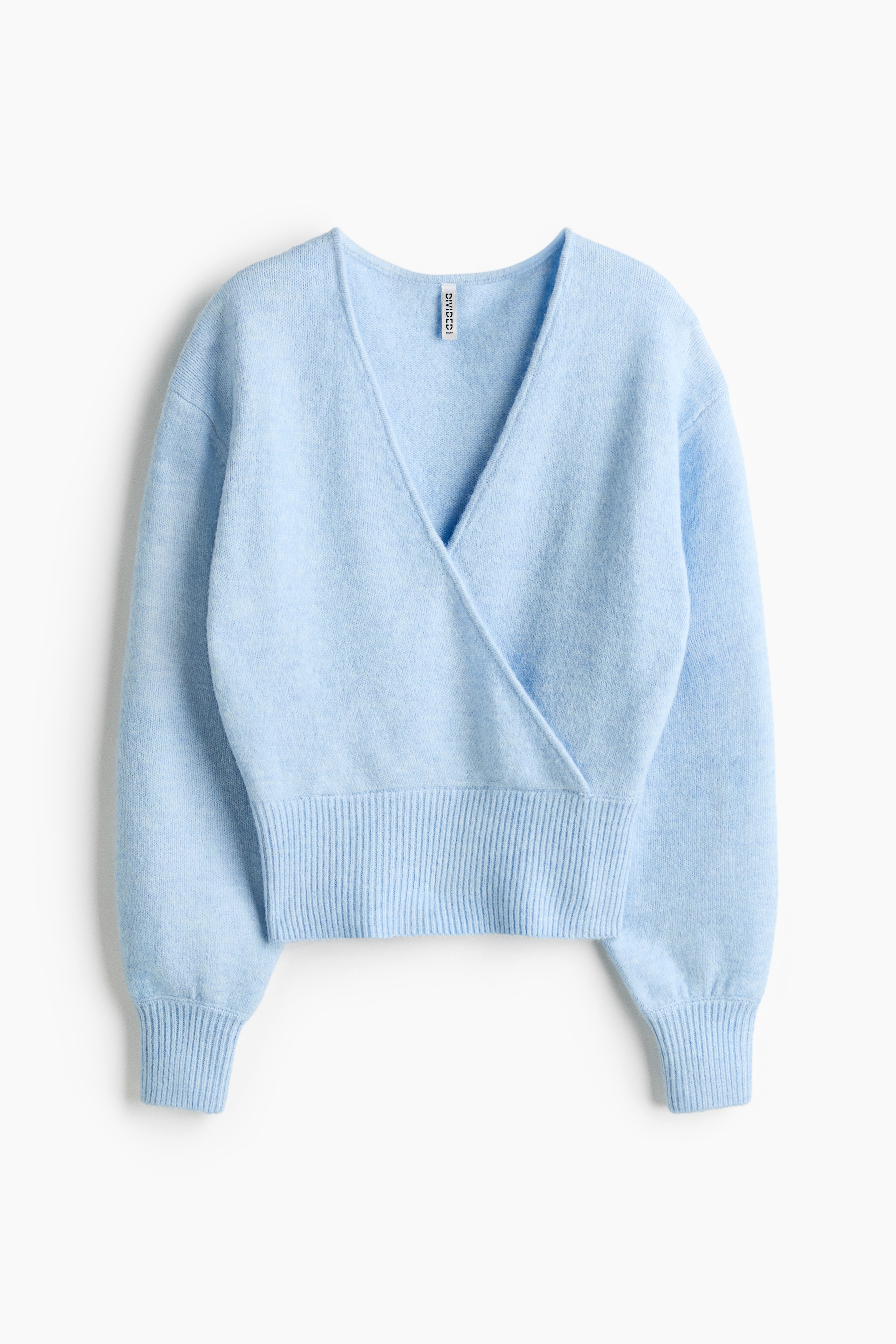 A light blue cropped wrap jumper is facing front, featuring a deep crossover V-neckline, long sleeves with ribbed cuffs, and a ribbed hem. The soft knit jumper is layered over a striped tank top, showcasing its relaxed fit and cropped length.