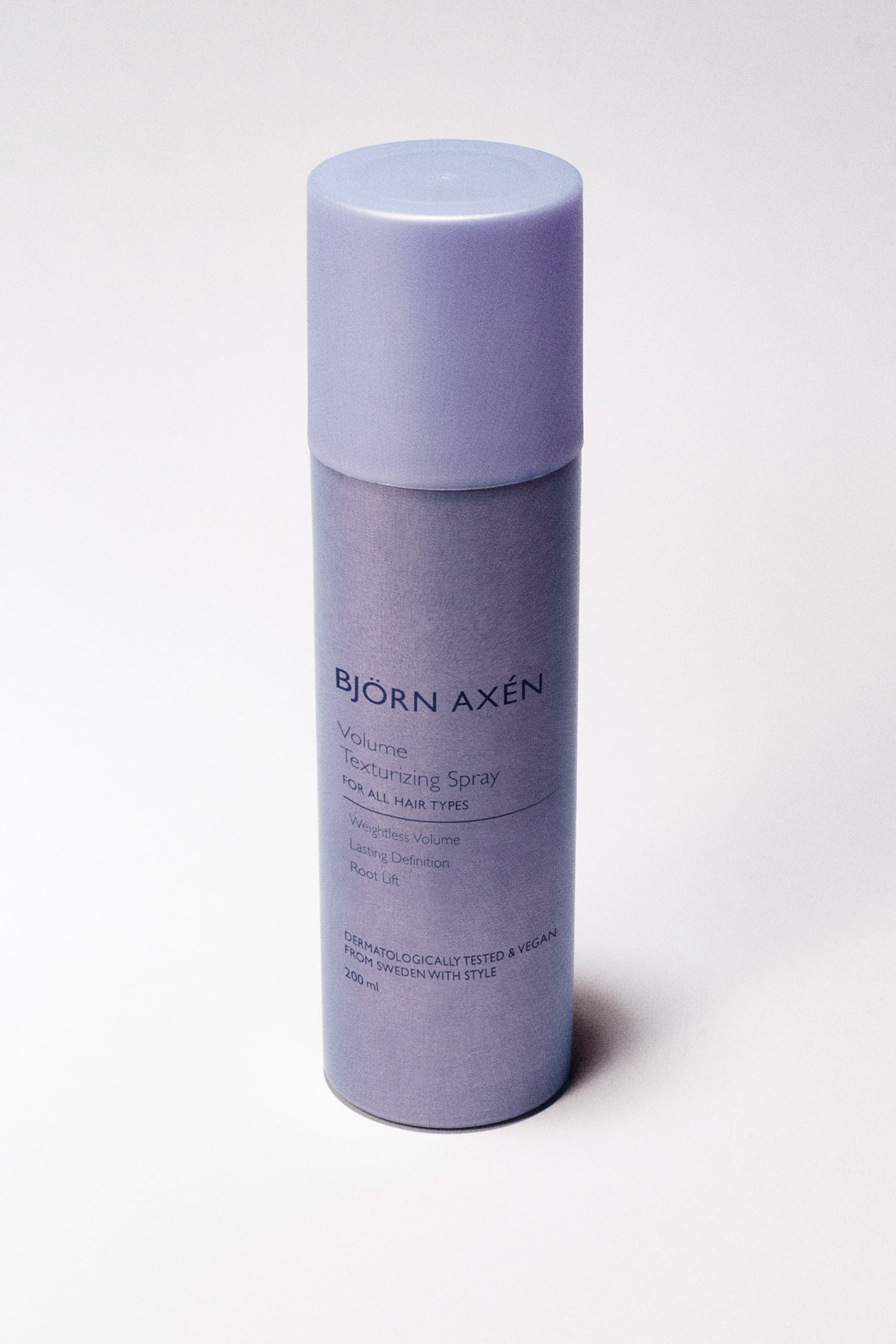 Vis større bilde: En sylindrisk lilla sprayflaske for hår står oppreist, vinklet litt til høyre. Den viser "BJÖRN AXÉN Volume Texturizing Spray for alle hårtyper" sammen med dens funksjoner og "200 ml" i hvit tekst.