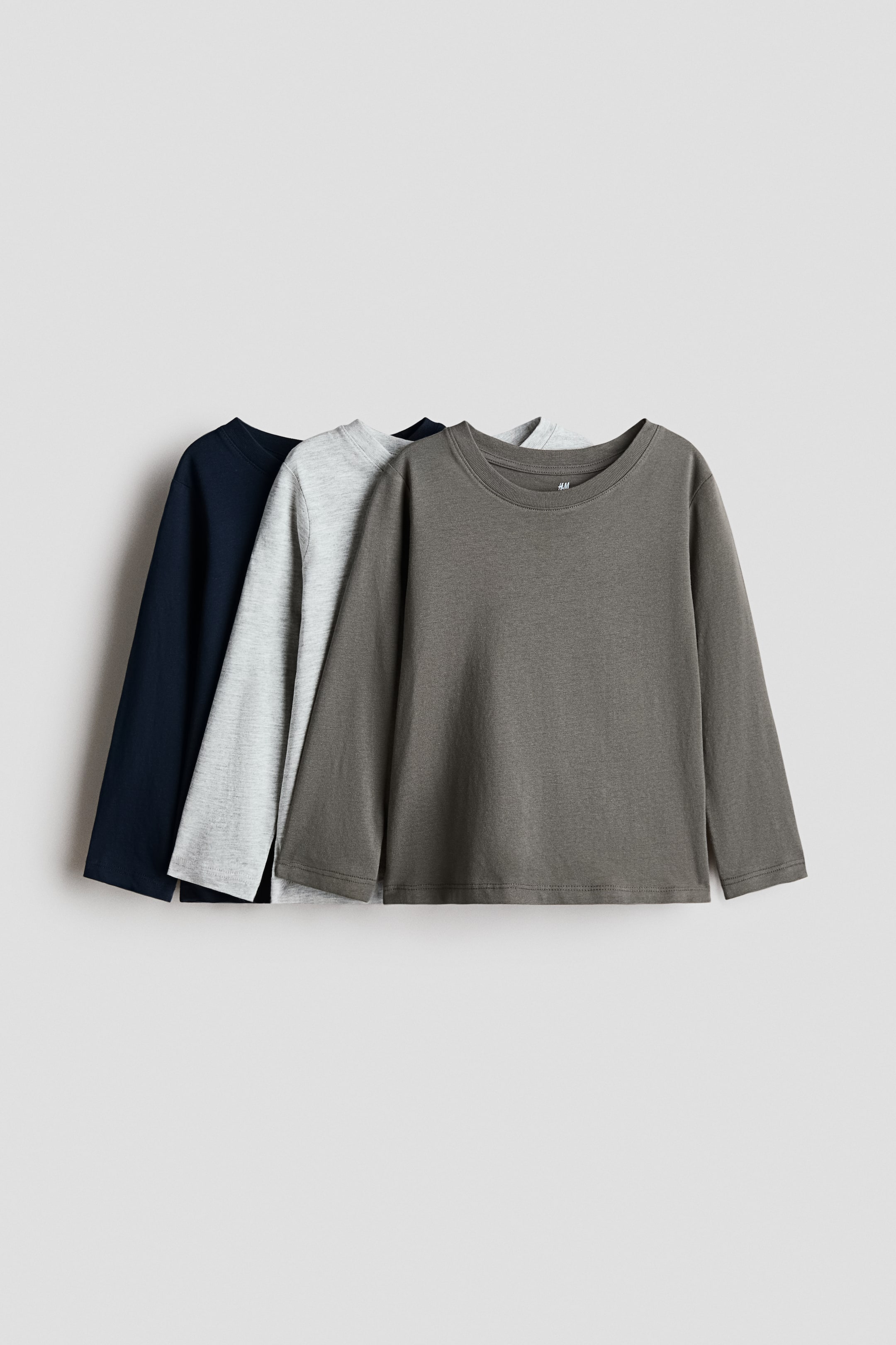 Ver imagen más grande: Tres camisetas de manga larga se presentan en una disposición en capas, con la camiseta delantera en verde oliva oscuro, una camiseta gris claro en el medio y una camiseta azul oscuro en la parte trasera. Cada camiseta cuenta con un cuello redondo y mangas largas.