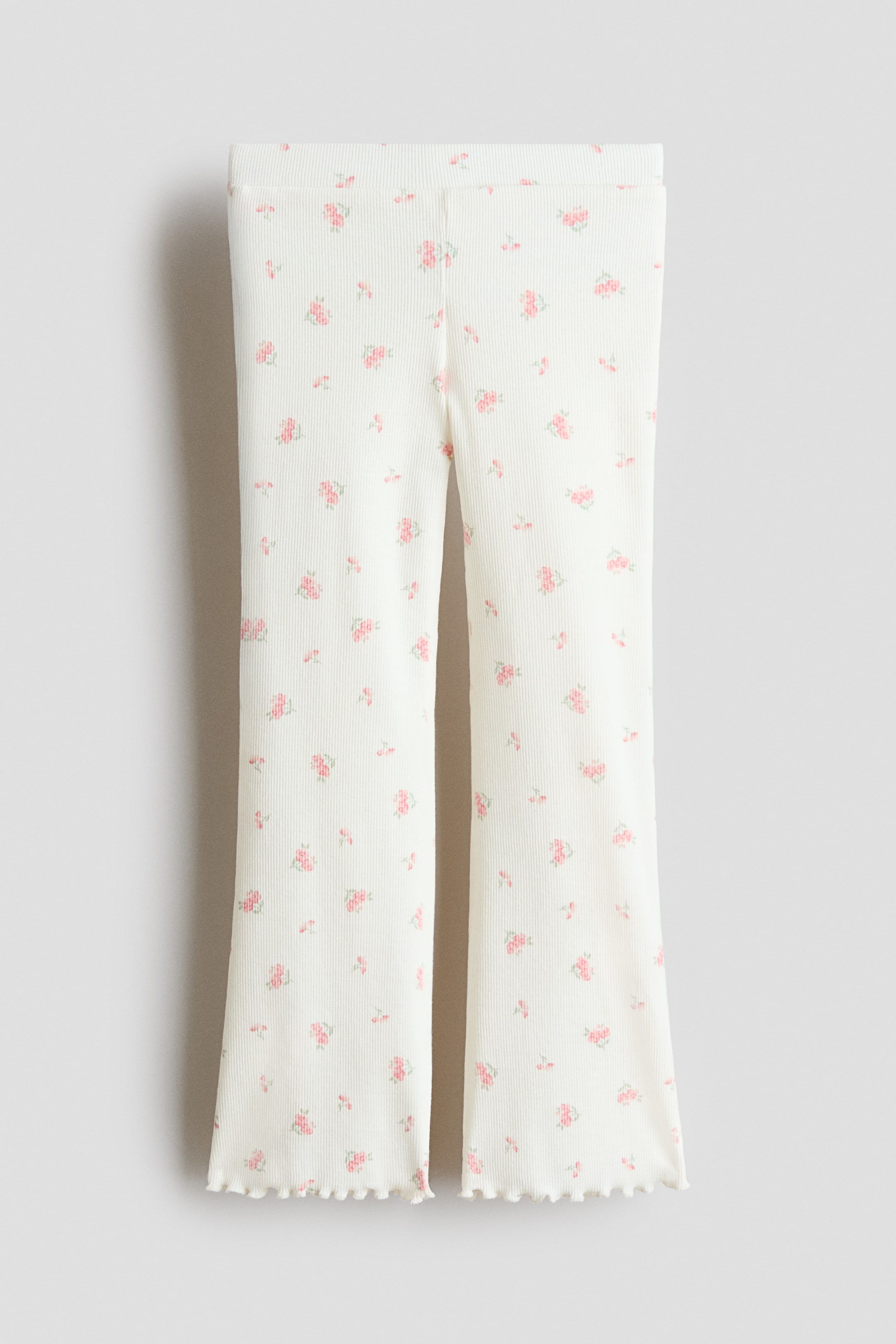 View larger image: Leggings are showcased in a front view, crafted from an off-white ribbed jersey fabric adorned with a scattered pink floral print. They feature a smooth waistband and flare at the legs, culminating in ruffled hems.