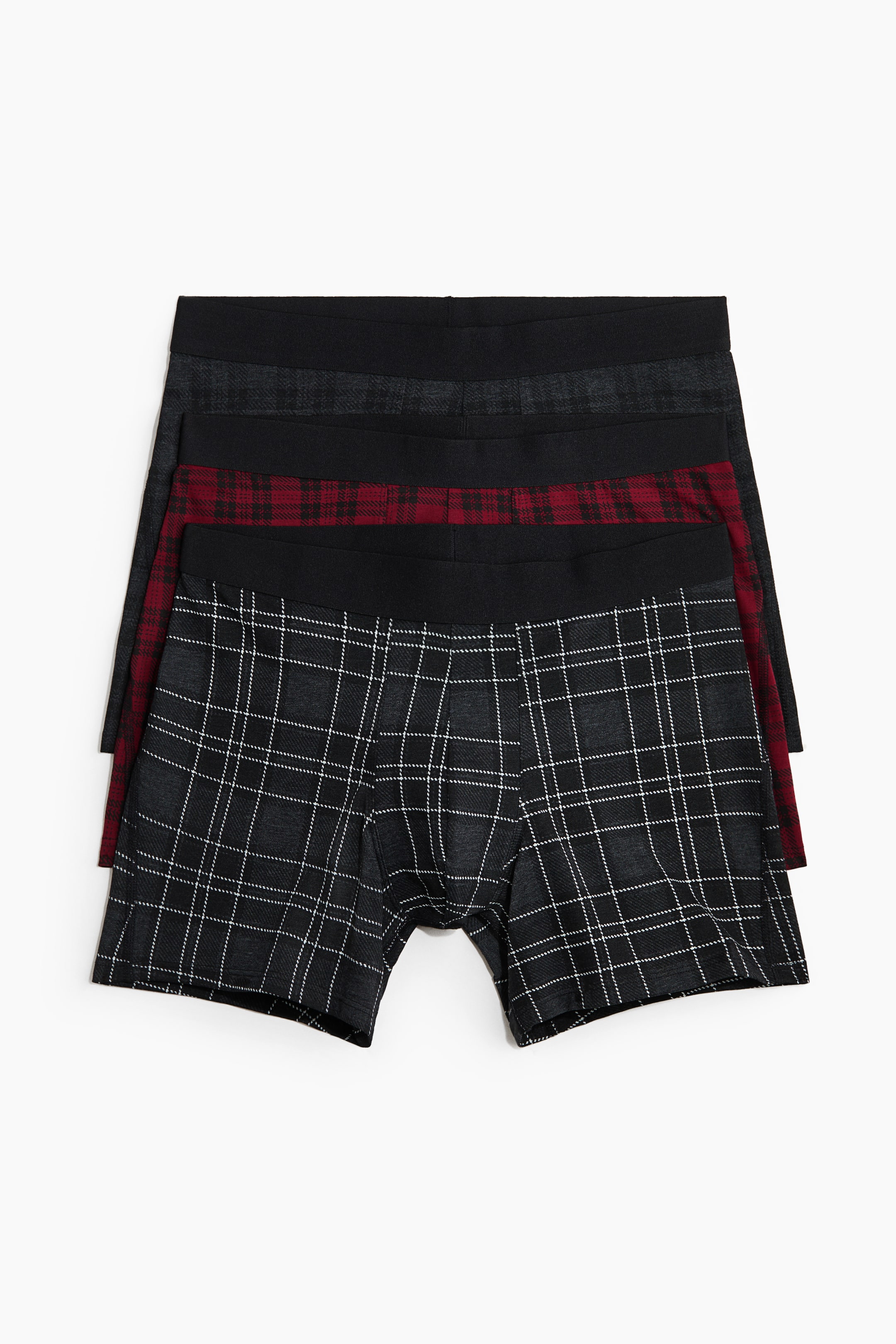 Grotere afbeelding bekijken: Een set van drie herenboxershorts ligt plat en recht naar voren, in een gelaagde stapel, waarbij elk paar een effen zwarte elastische tailleband heeft. Het voorste paar toont een donkergrijs en wit ruitpatroon, het middelste paar een rood en zwart ruitpatroon, en het achterste paar een donkergrijs ruitpatroon.