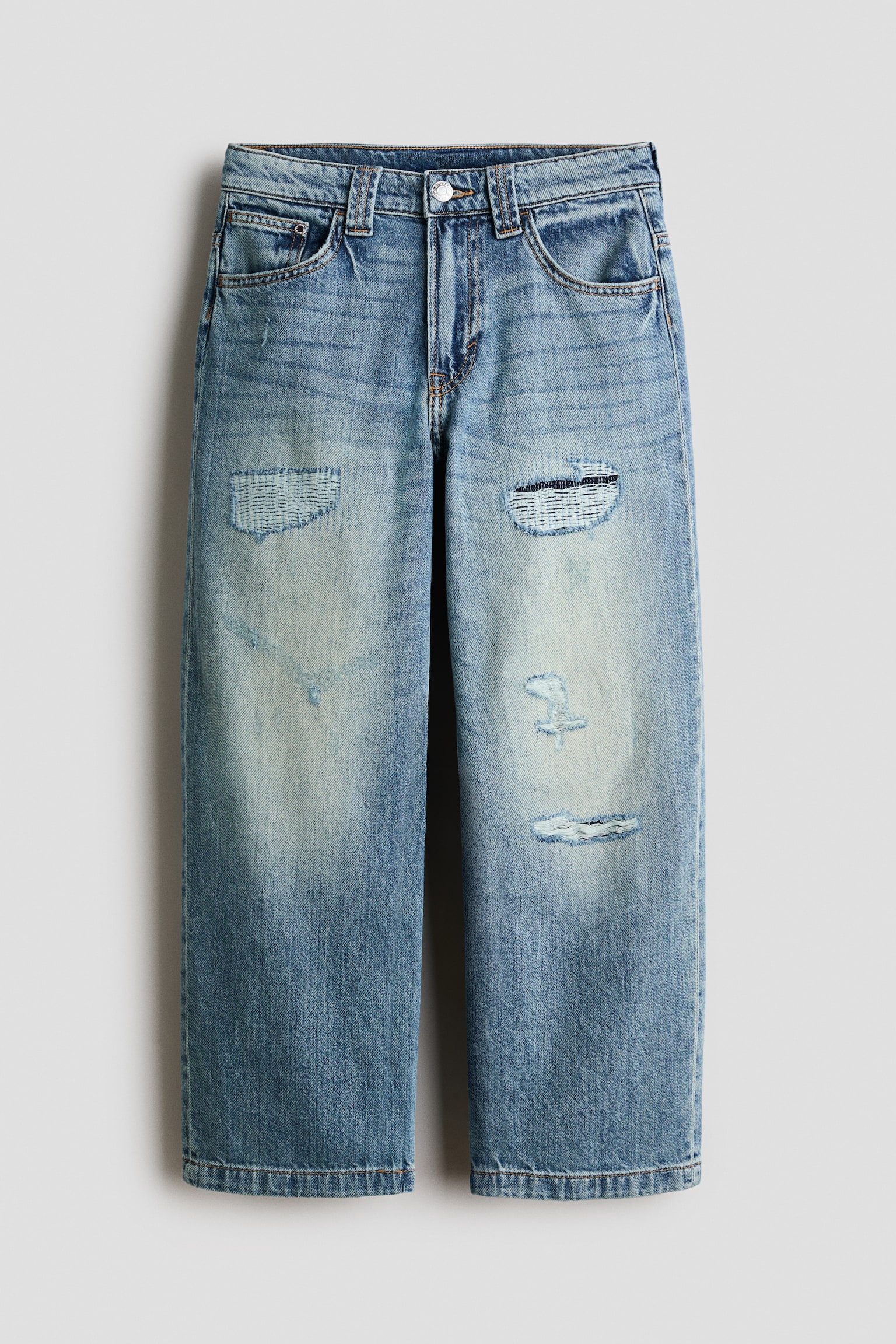 Ce jean en denim bleu dÃ©lavÃ© Ã  coupe ample est prÃ©sentÃ© de face, avec une coupe droite Ã  jambe large, une fermeture Ã  bouton et une braguette zippÃ©e. Le jean prÃ©sente des dÃ©tails dÃ©lavÃ©s sur les cuisses ainsi que des Ã©lÃ©ments usÃ©s, notamment des empiÃ¨cements texturÃ©s rÃ©parÃ©s et des dÃ©chirures effilochÃ©es sur les deux jambes.