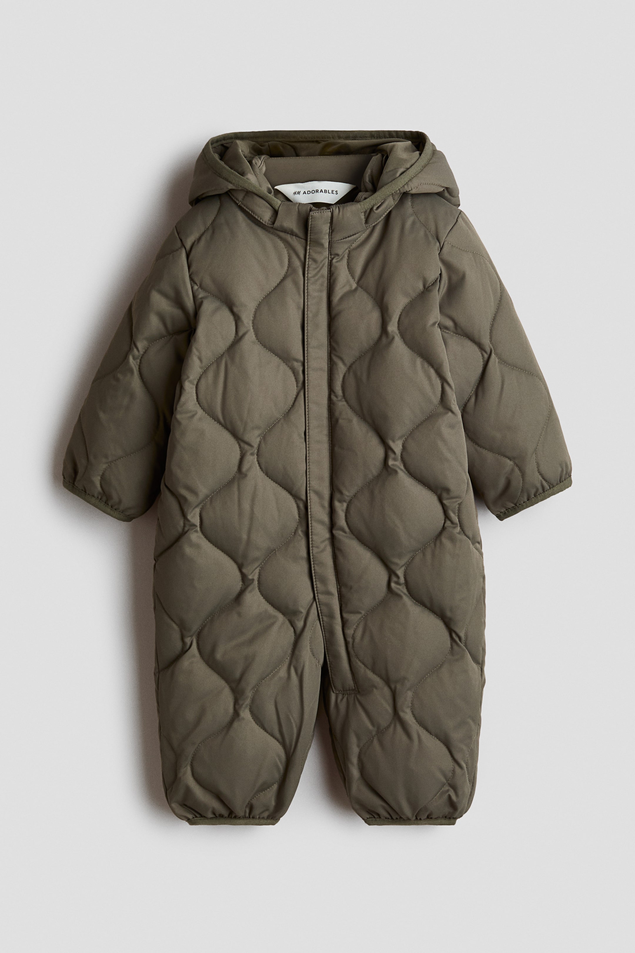Grotere afbeelding bekijken: Een olijfgroene H&M Adorables sneeuwpak is van voren te zien, met een gewatteerde weefstructuur met een afgerond patroon. Het is ontworpen met een капuuchon, een verborgen ritssluiting die langs de voorkant en één pijp loopt, en jerseyboorden aan de manchetten en zomen.