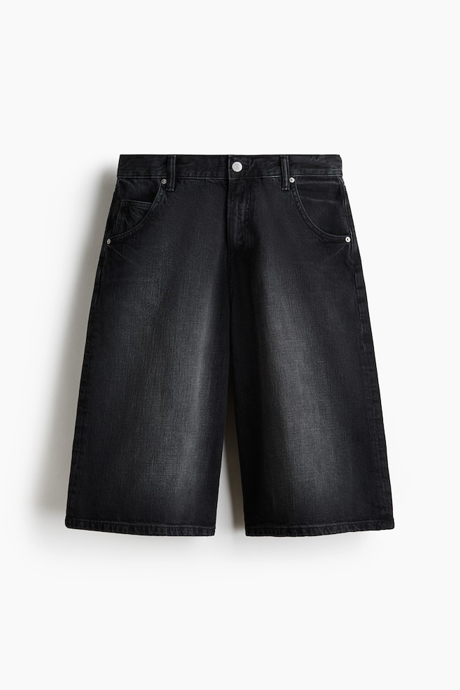 Estos shorts de mezclilla rígida de algodón negro se muestran de frente, con una cintura regular, cierre de cremallera y un único botón plateado. Presentan dos bolsillos frontales redondeados con remaches metálicos y un pequeño bolsillo para monedas, además de un ajuste holgado, piernas redondeadas y amplio espacio alrededor del muslo. - 1