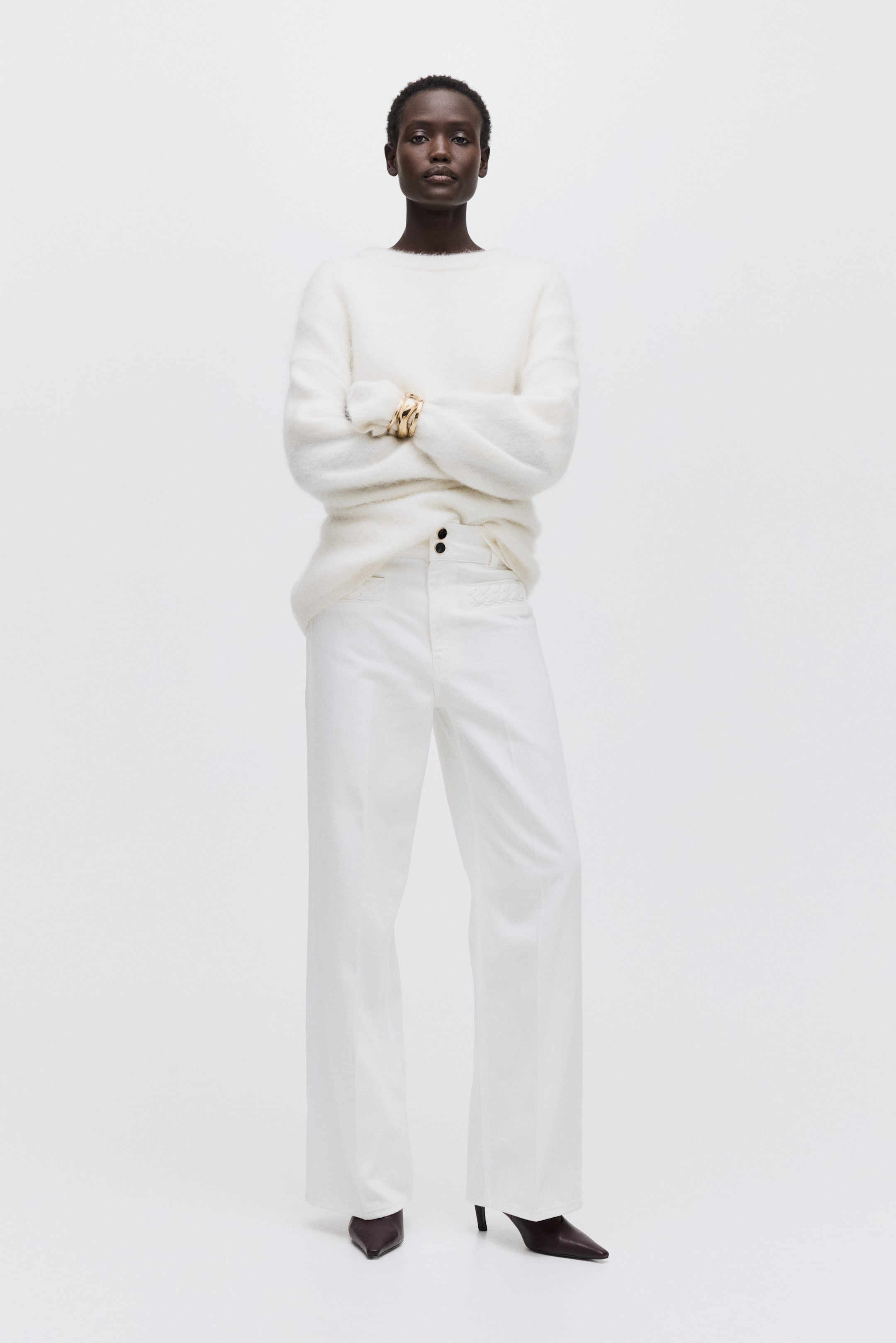 Voir une image plus grande: Un chandail blanc pelucheux à col rond est présenté de face, avec des manches longues et une coupe décontractée. Un pantalon blanc à jambes larges est également présenté, avec une taille haute dotée de deux boutons noirs visibles et des coutures décoratives subtiles à l'avant.