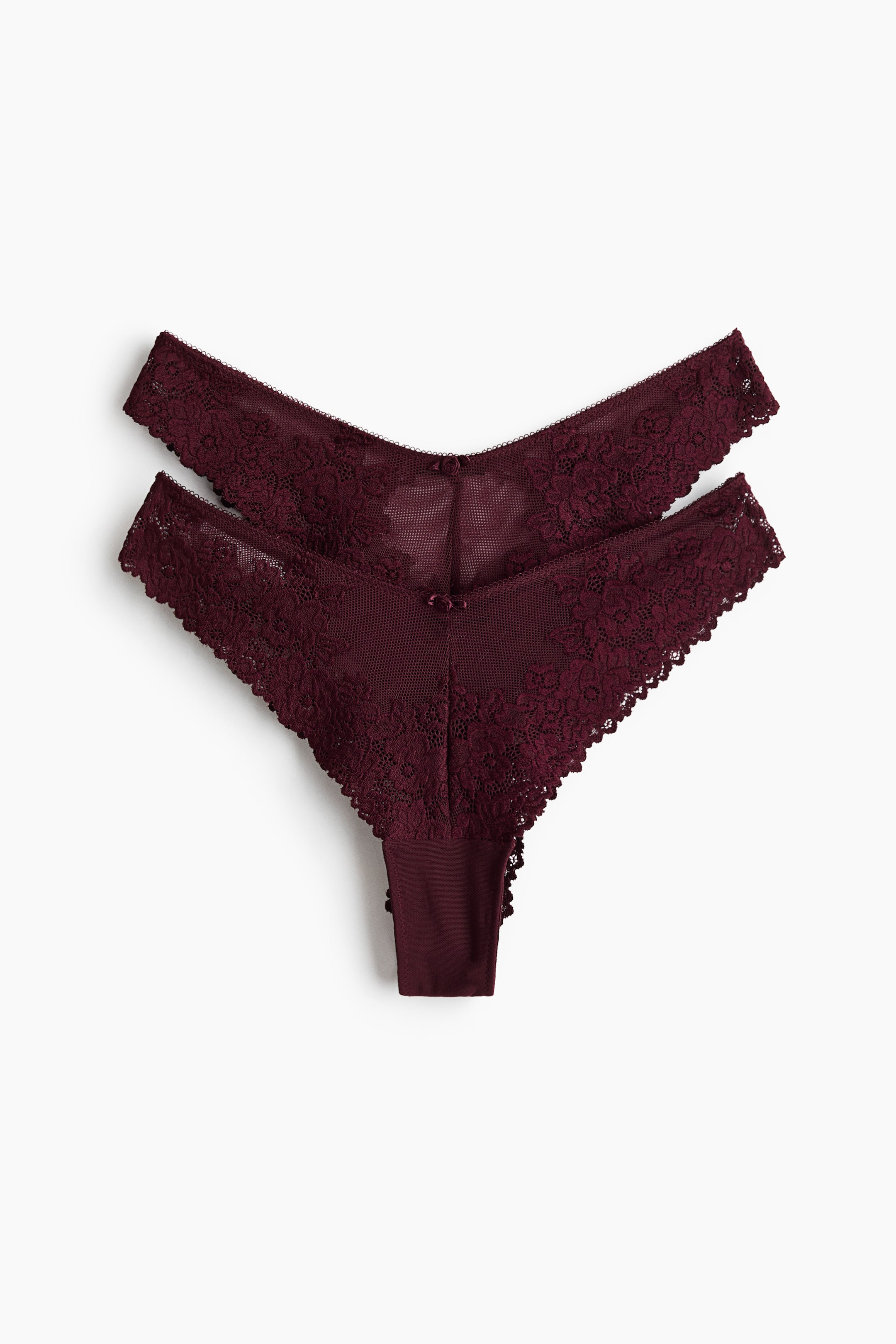 View larger image: Two burgundy thongs are layered, one slightly over the other. They feature intricate lace detailing and mesh fabric, with scalloped lace edges and a small bow accenting the front centre of each.