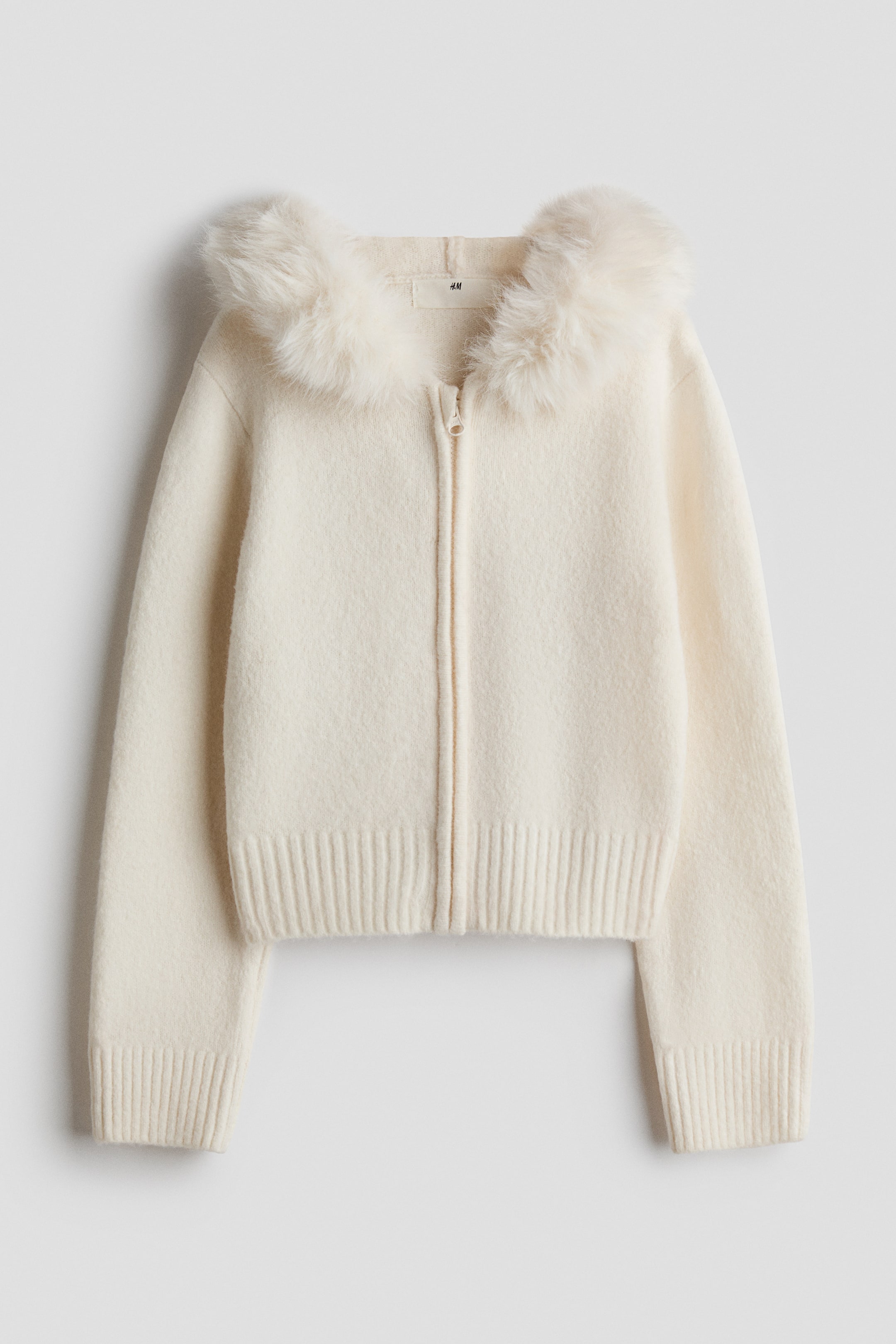 View larger image: A cream hooded zip-up cardigan is facing front, featuring a fluffy faux fur lining around its hood, a full-length zipper closure, ribbed cuffs, and a ribbed hem.
