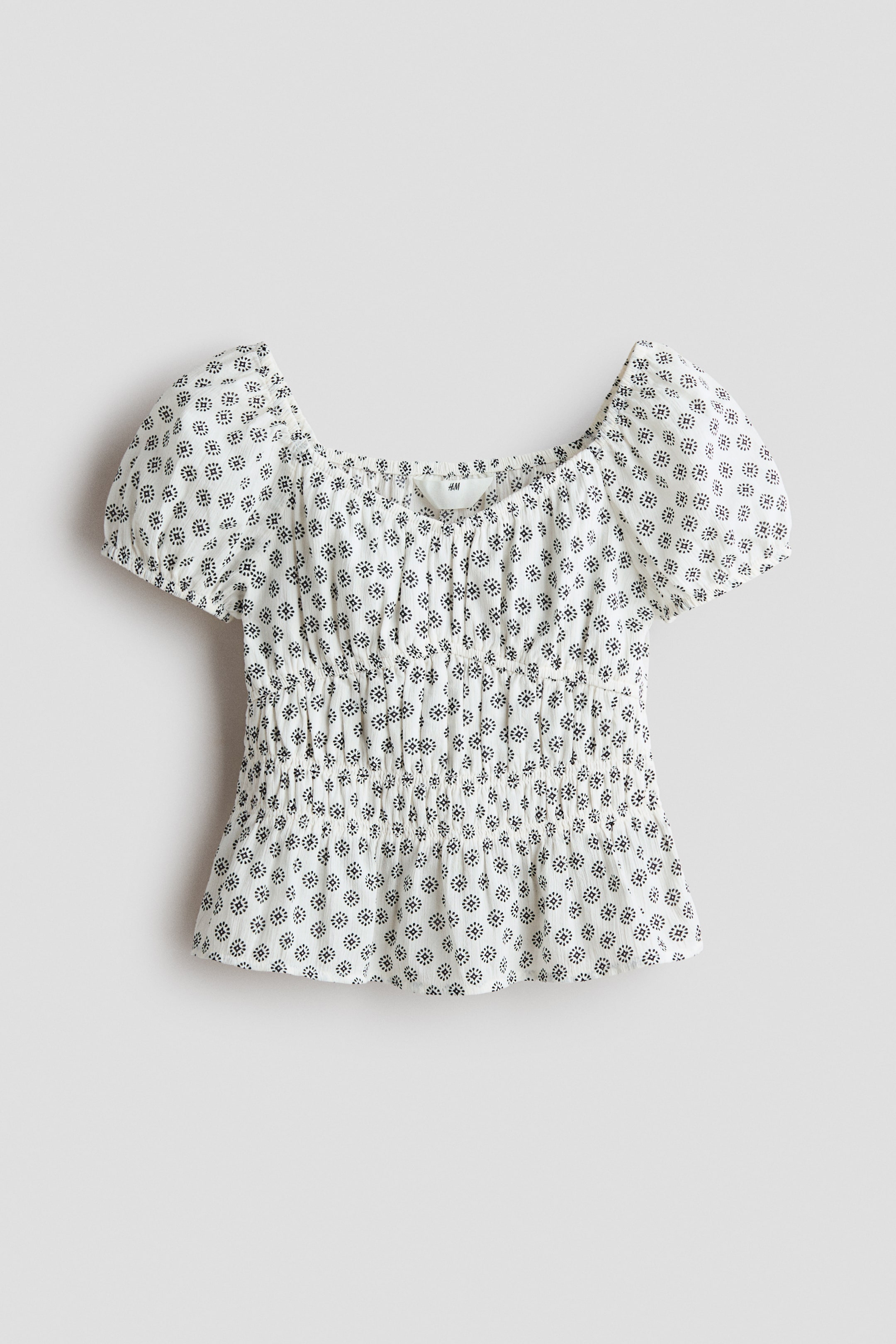 View larger image: The top is white with a repeating black dot pattern, featuring a square neckline and puffed short sleeves. It showcases smocking details across the midsection, creating a fitted and gathered silhouette.
