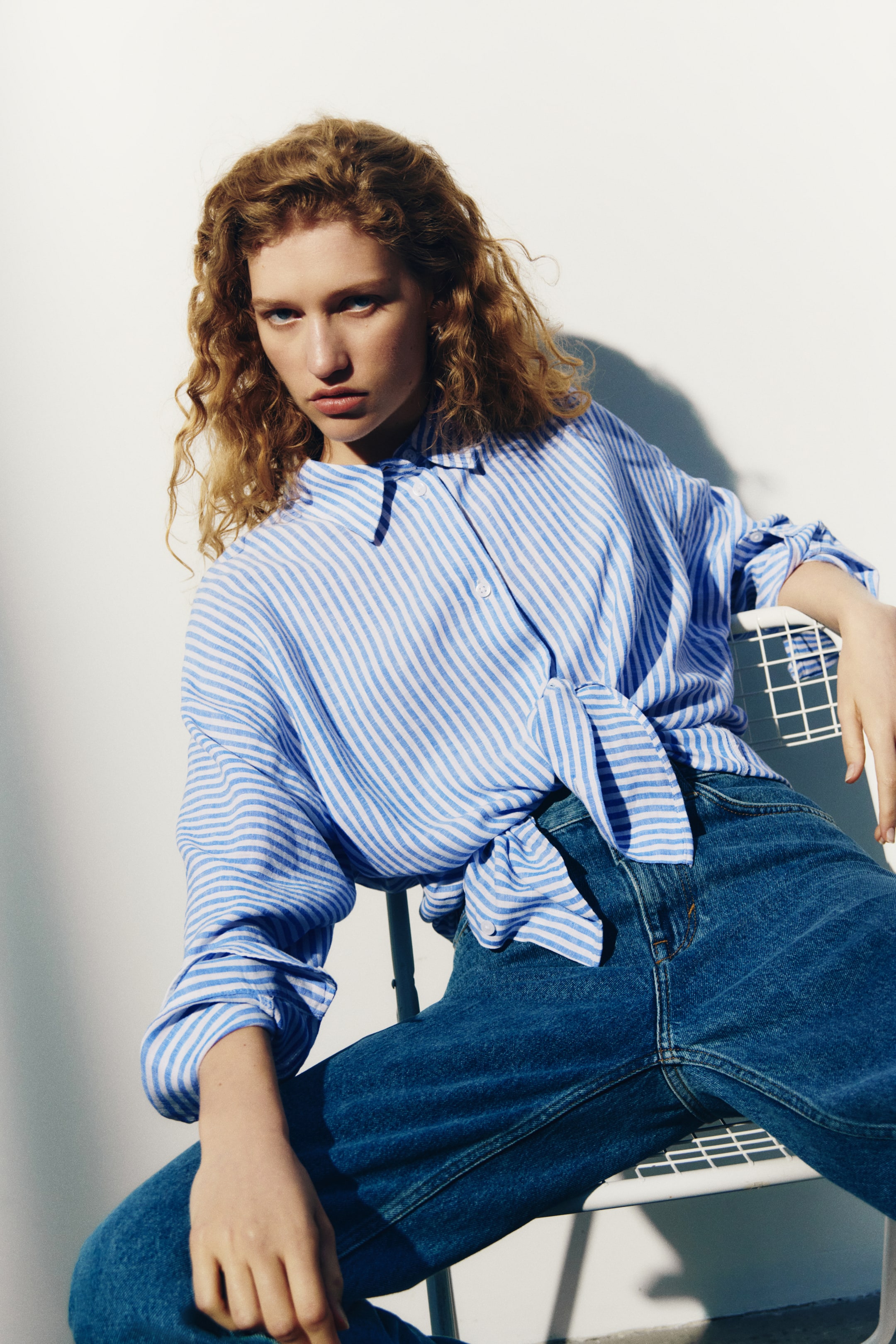Visualizza immagine più grande: La modella indossa una camicia a righe oversize con colletto e bottoni frontali. La camicia, caratterizzata da spalle scese e maniche lunghe con polsini, è annodata in vita sopra i jeans.