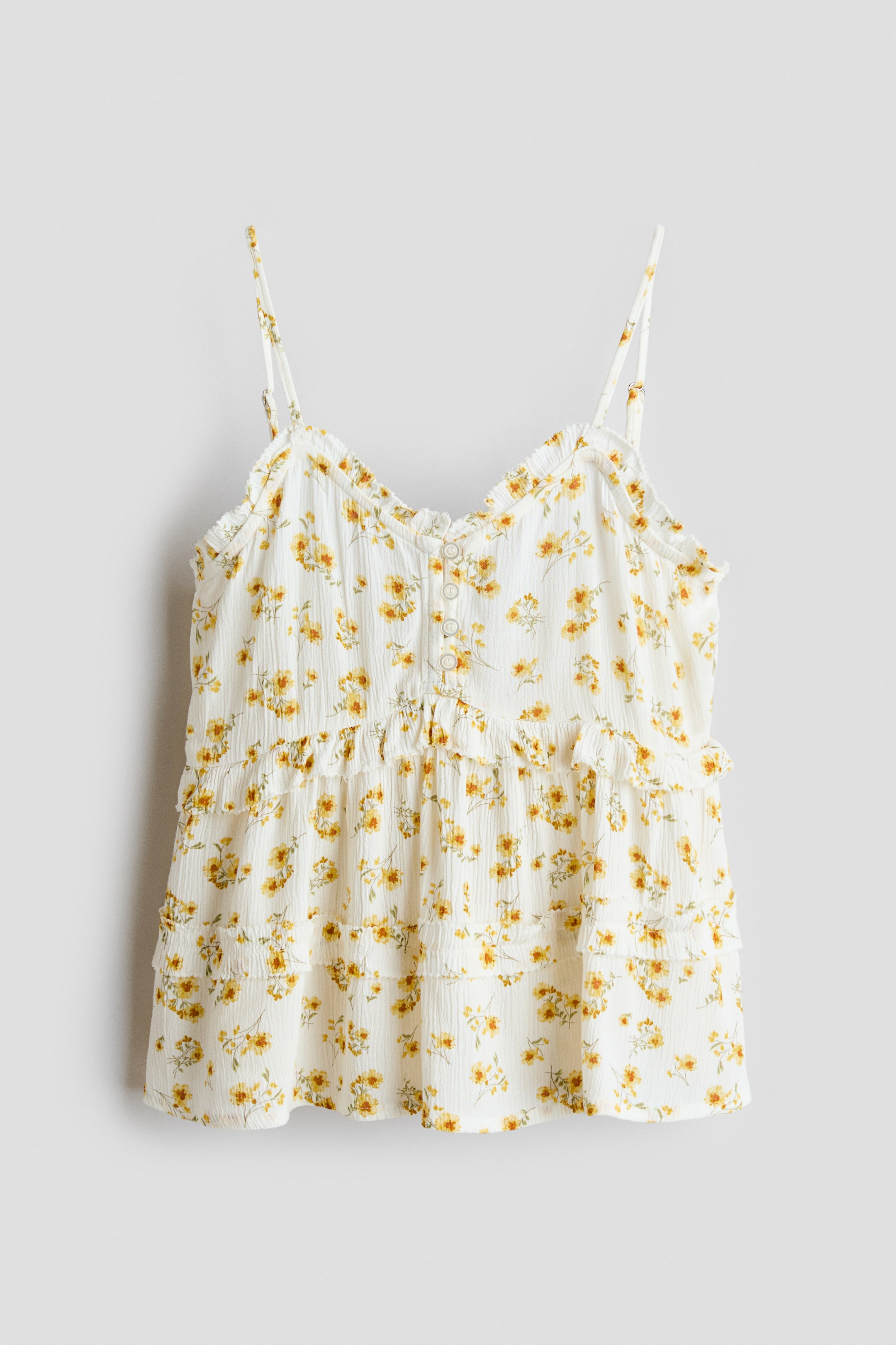 View larger image: The white camisole top showcases a yellow floral pattern, thin spaghetti straps, and a ruffled V-neckline. It also features a partial button placket at the front and tiered ruffles on its relaxed body.