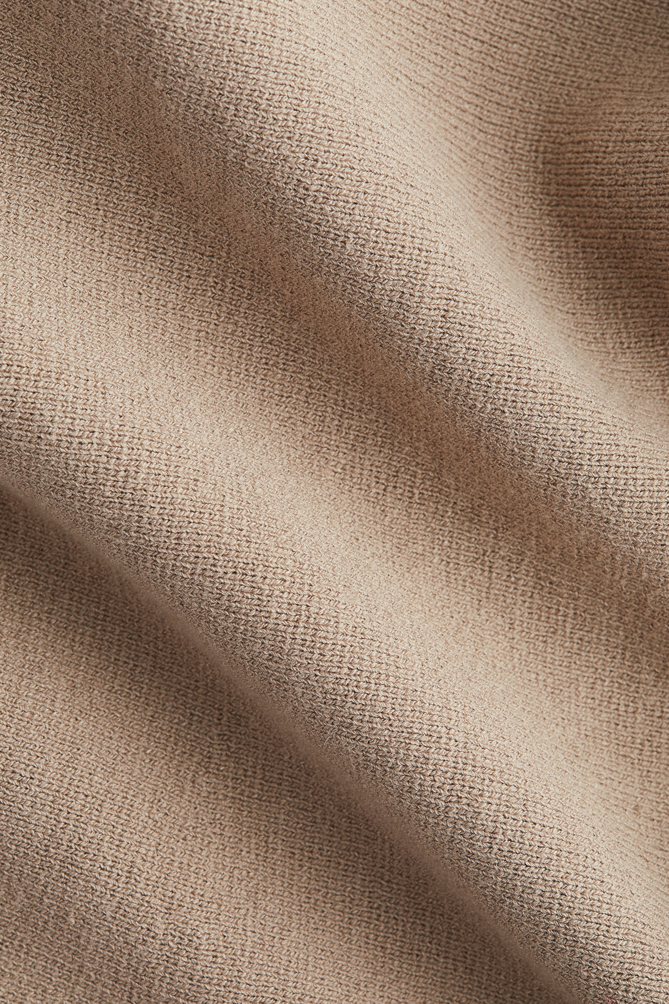 Agrandir l'image: Un tissu tricoté beige présente un tissage texturé avec des plis doux et drapés.