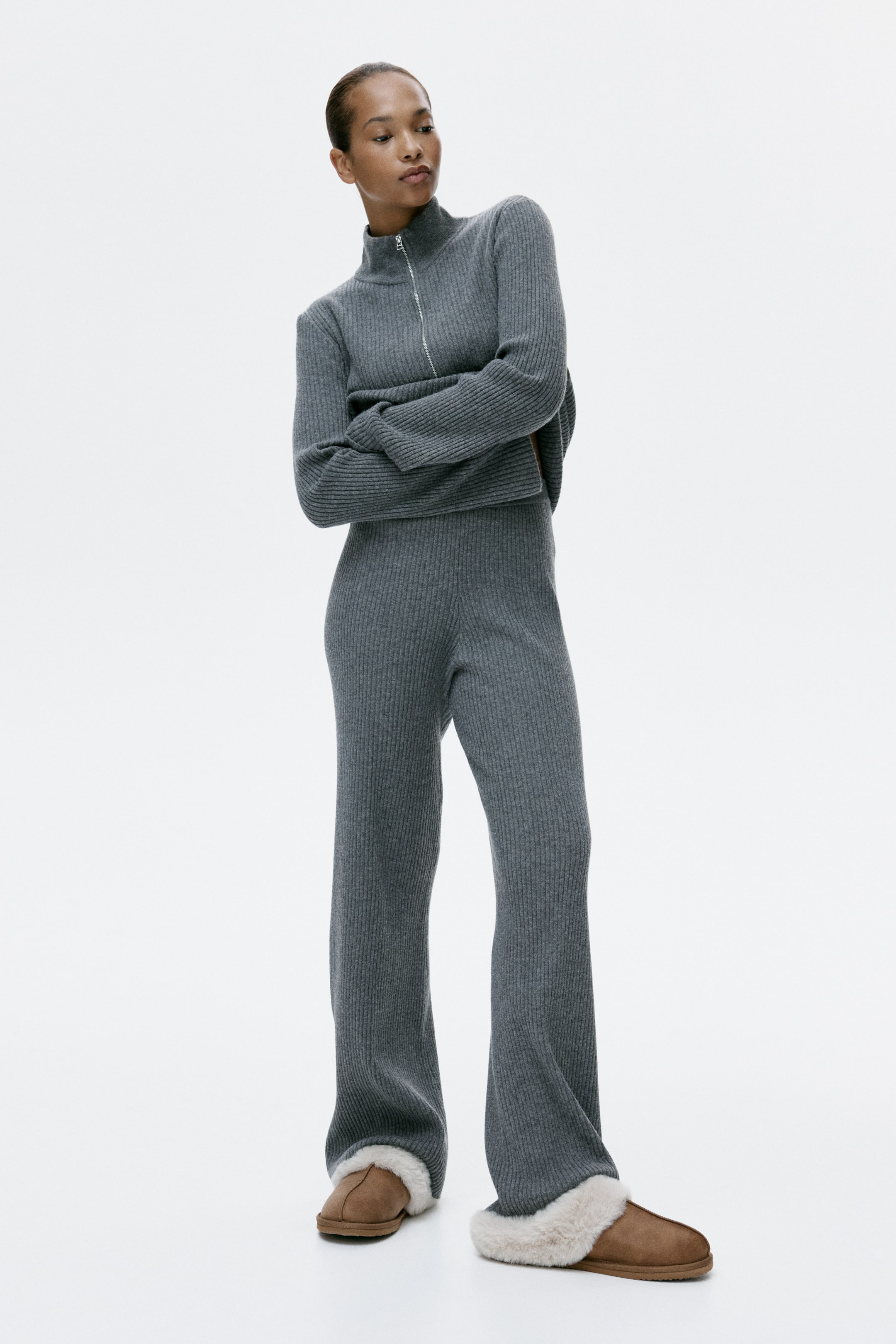 拡大画像を表示: グレーのリブニット2ピースセットをフロントの3/4ビューでご紹介しています。セットはクロップ丈のクォータージップタートルネックトップ（長袖）と、ハイウエストのワイドレッグパンツで構成されています。