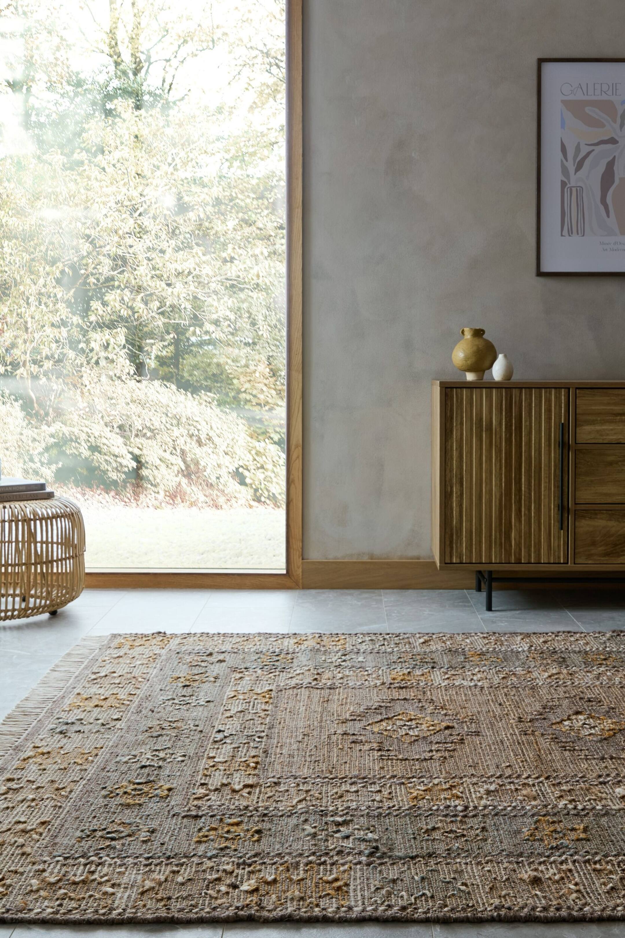 Visualizza immagine più grande: Il tappeto presenta un motivo geometrico in tonalità terrose di marrone, beige e giallo. Mostra una superficie strutturata con sezioni tessute piatte e dettagli rialzati ad anello, e presenta frange lungo il bordo sinistro.