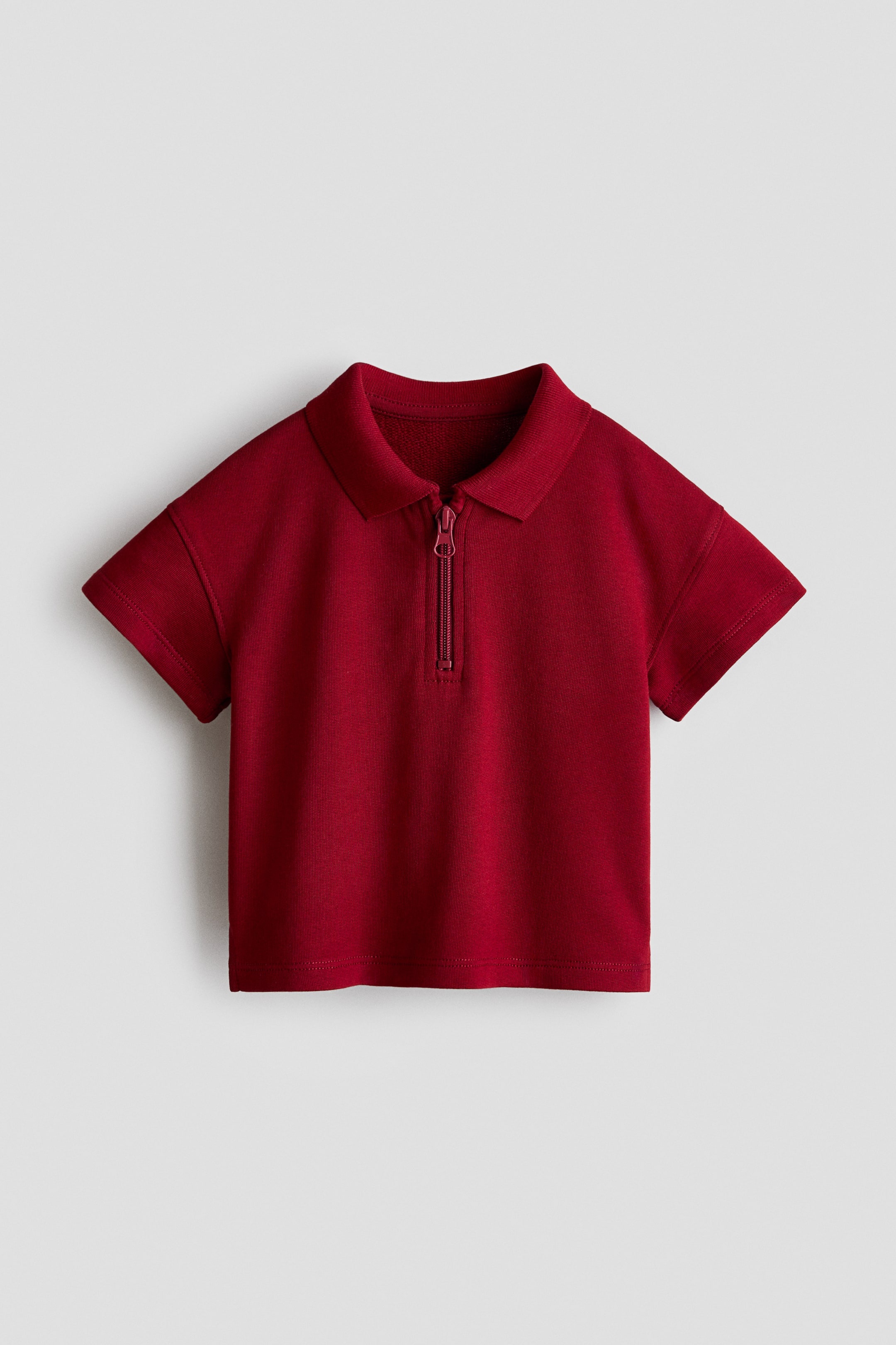 View larger image: A deep red polo shirt is displaying its front view, featuring a classic collar and a quarter-zip placket. It is showcasing short sleeves and a straight hem.