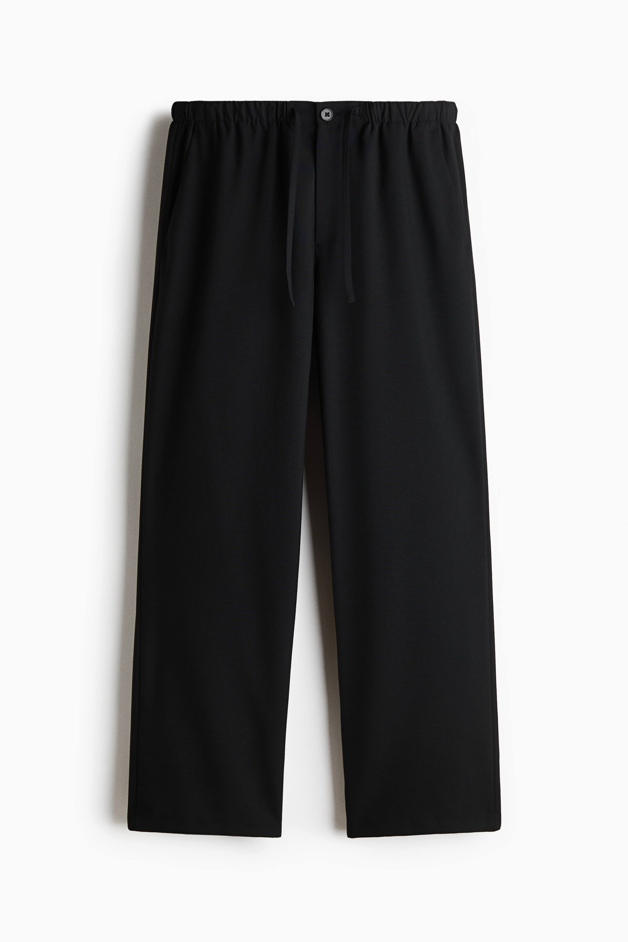View larger image: Black trousers are displayed hanging front-facing, featuring an elasticated waistband with a central button closure and adjustable drawstrings. The trousers showcase a relaxed, straight-leg silhouette with a smooth fabric finish.