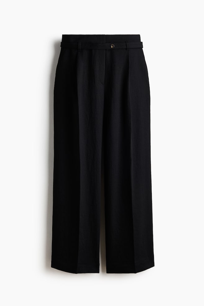 Black wide-leg trousers are showcasing a textured fabric, featuring front pleats, a plain waistband with belt loops, and a single brown button fastening the front. - 1