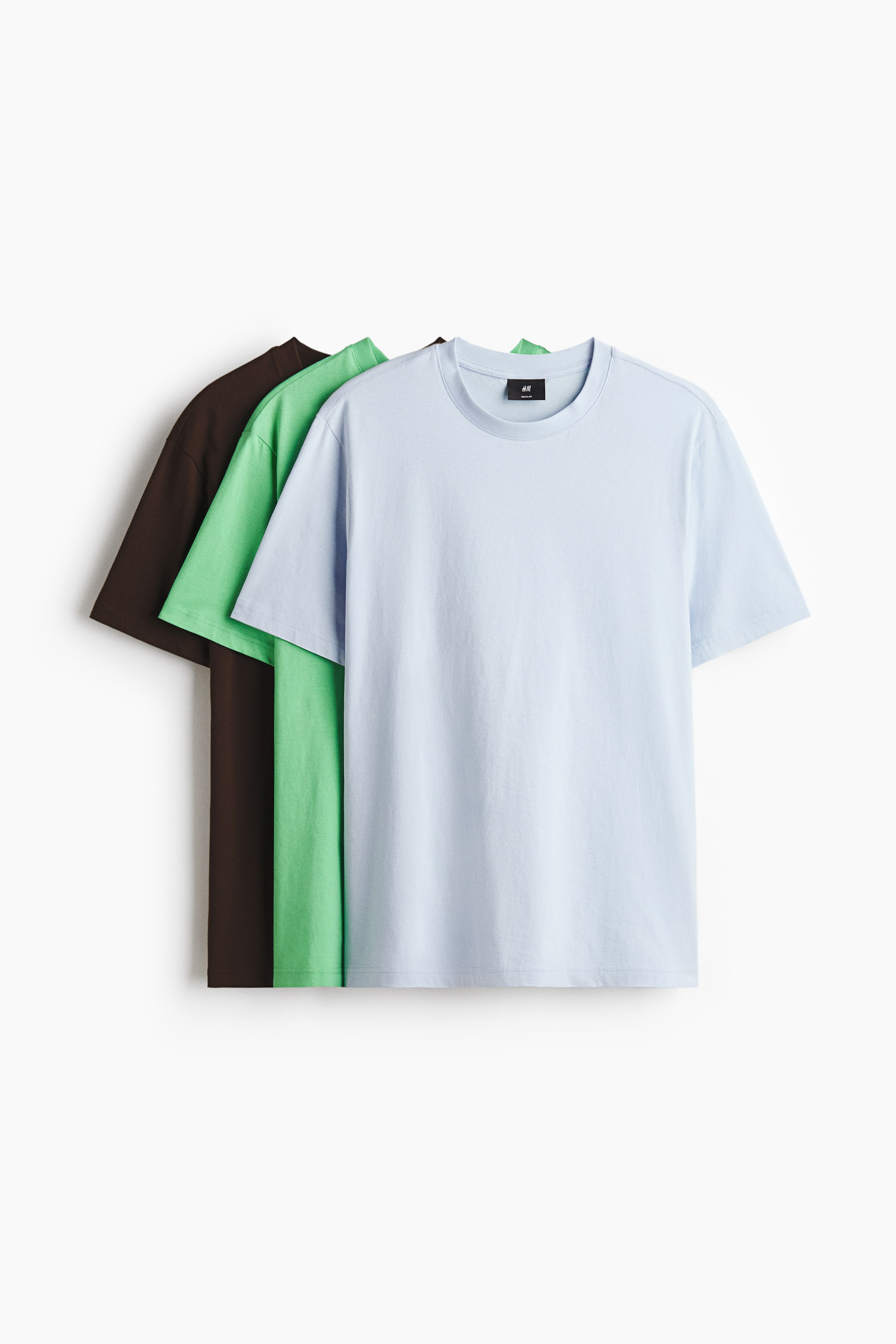 View larger image: Three t-shirts are displayed, layered with the front of a light blue t-shirt showcasing its round, rib-trimmed neckline, short sleeves, and straight-cut hem. A light green t-shirt and a dark brown t-shirt are partially visible behind it.