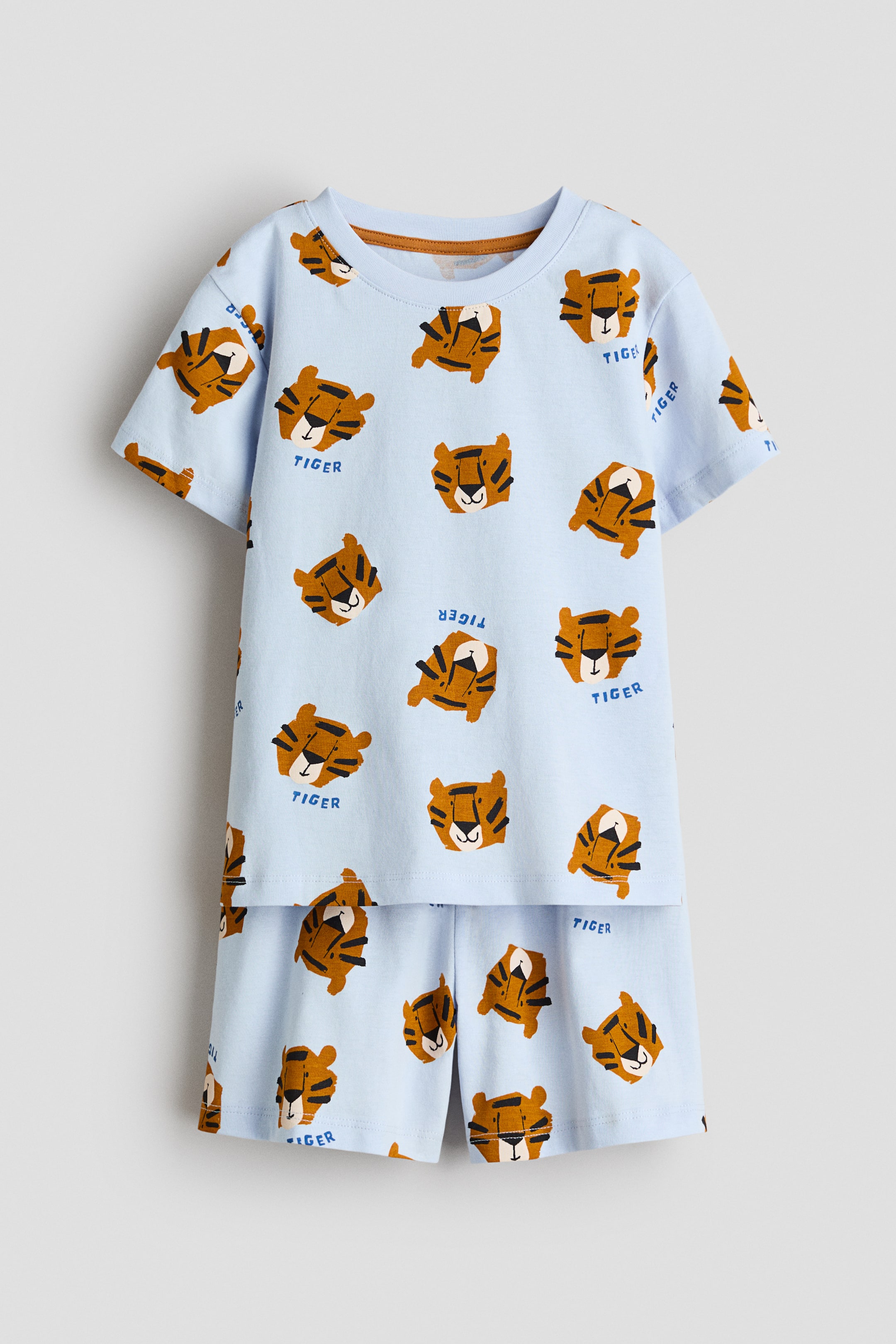 Ver imagem maior: Pijamas em suave jersey de algodão estampado são exibidos de frente, apresentando uma t-shirt azul clara com acabamento canelado em torno da gola e calções a condizer com cintura elástica. Ambas as peças exibem um padrão completo de caras de tigres de desenho animado e a palavra 'TIGER'.