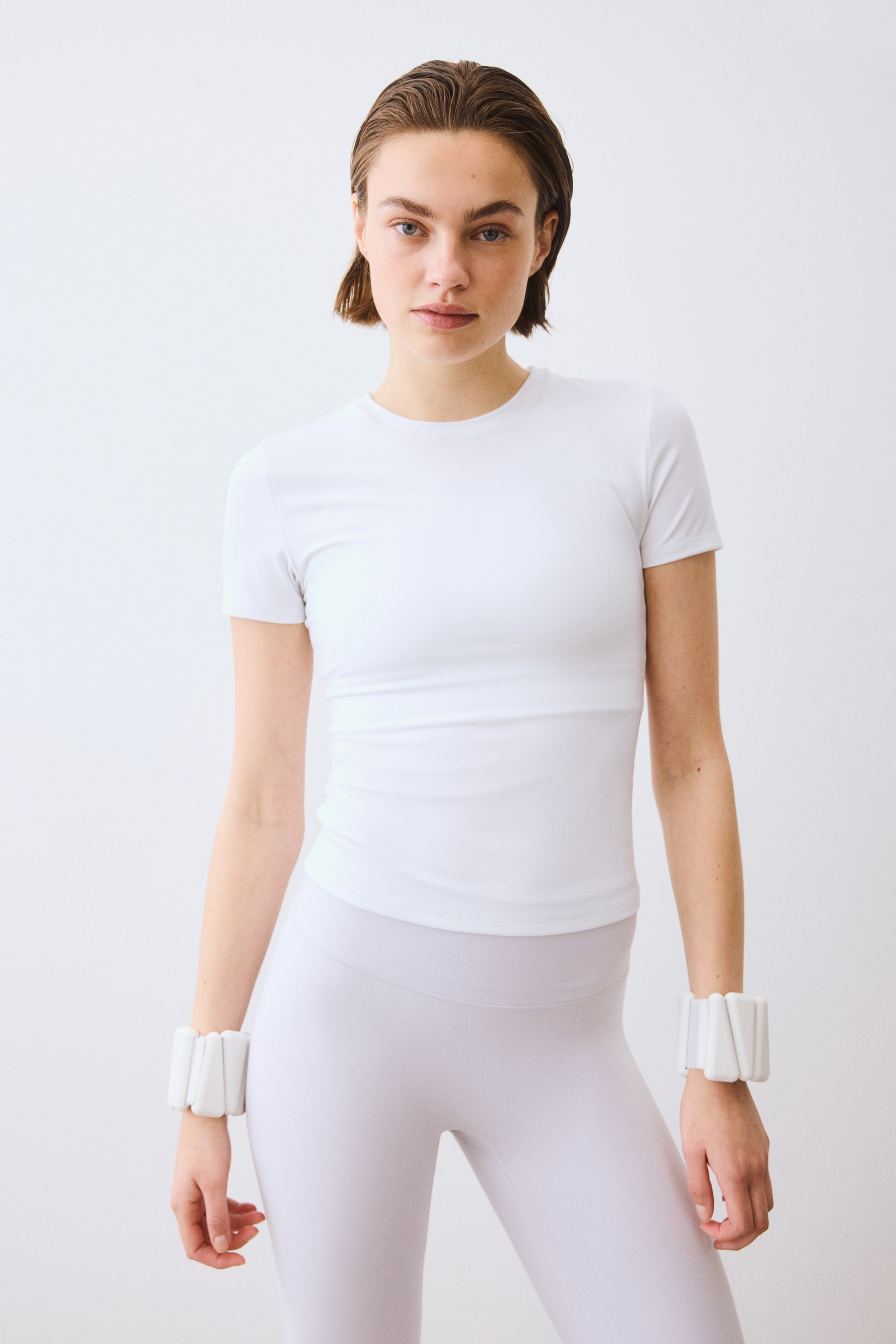 拡大画像を表示: ラウンドネックラインとフィット感のあるデザインが特徴の、白いフィットした半袖Tシャツ。