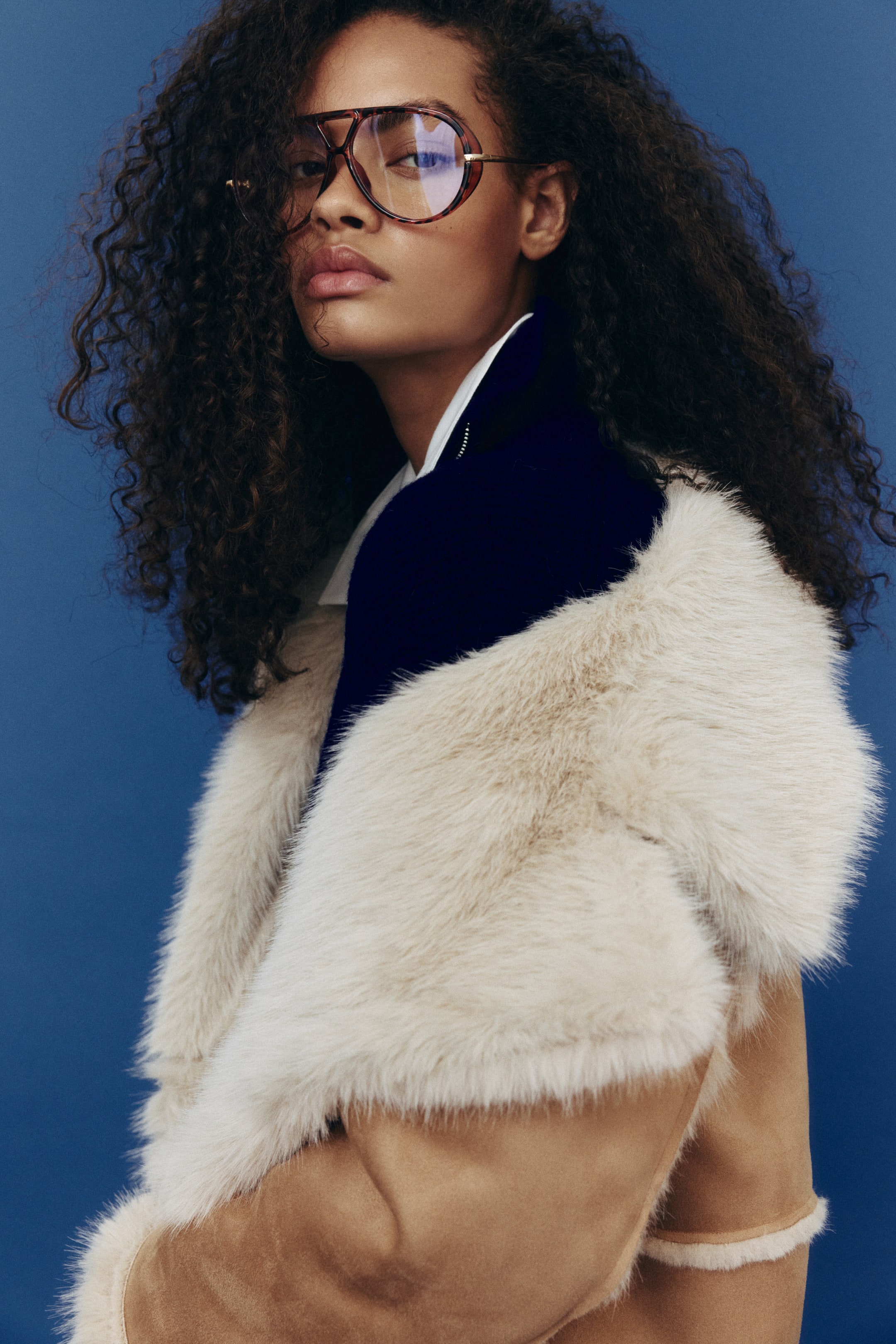 Agrandir l'image: Un manteau avec une finition douce et duveteuse de couleur brun clair et des garnitures et une doublure crème moelleuses est porté ouvert par le mannequin, révélant un vêtement foncé en dessous.