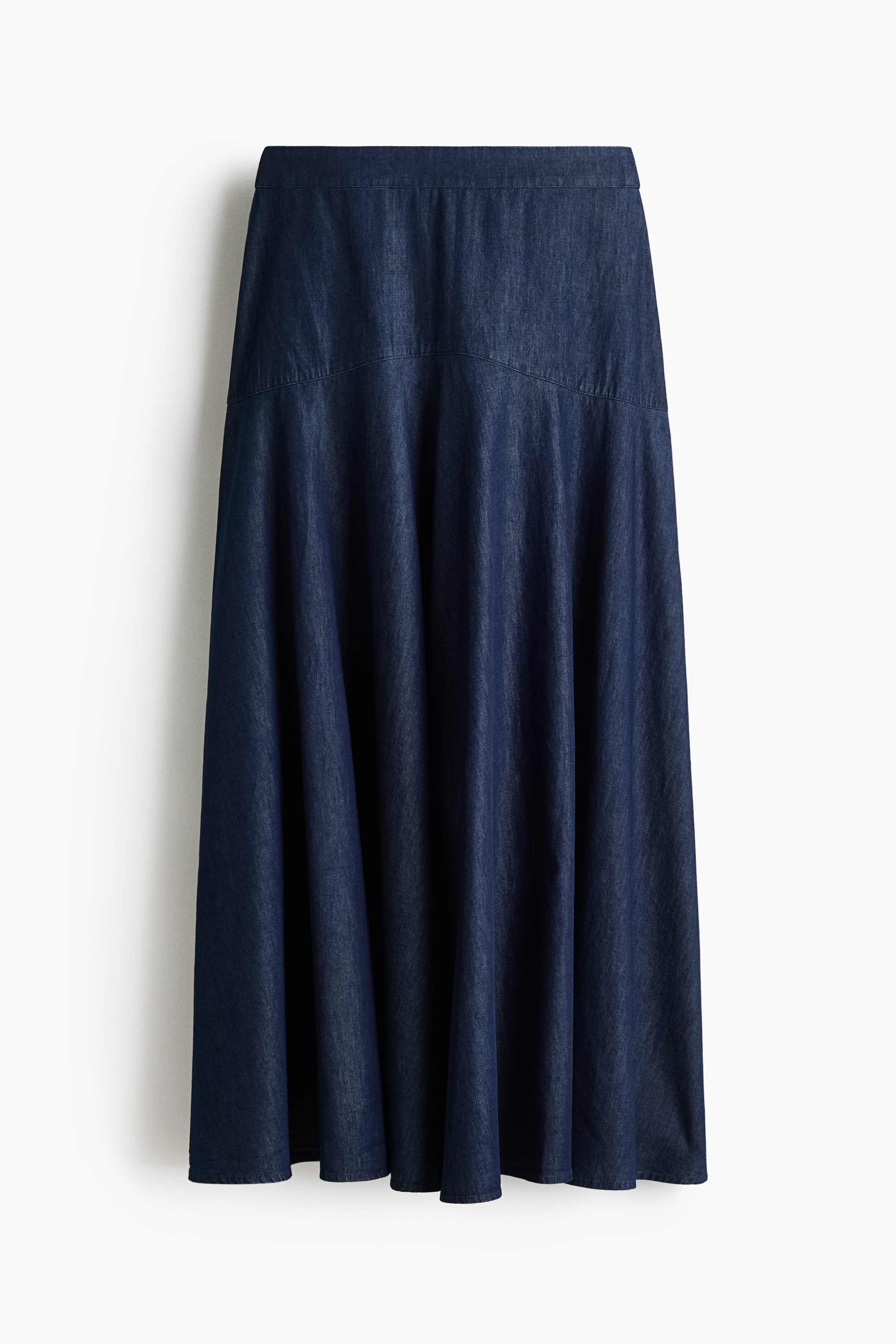View larger image: A dark-blue denim skirt is shown from the front, featuring a flat waistband and a curved yoke panel. The skirt gently flares from the yoke into soft pleats down to the hem.