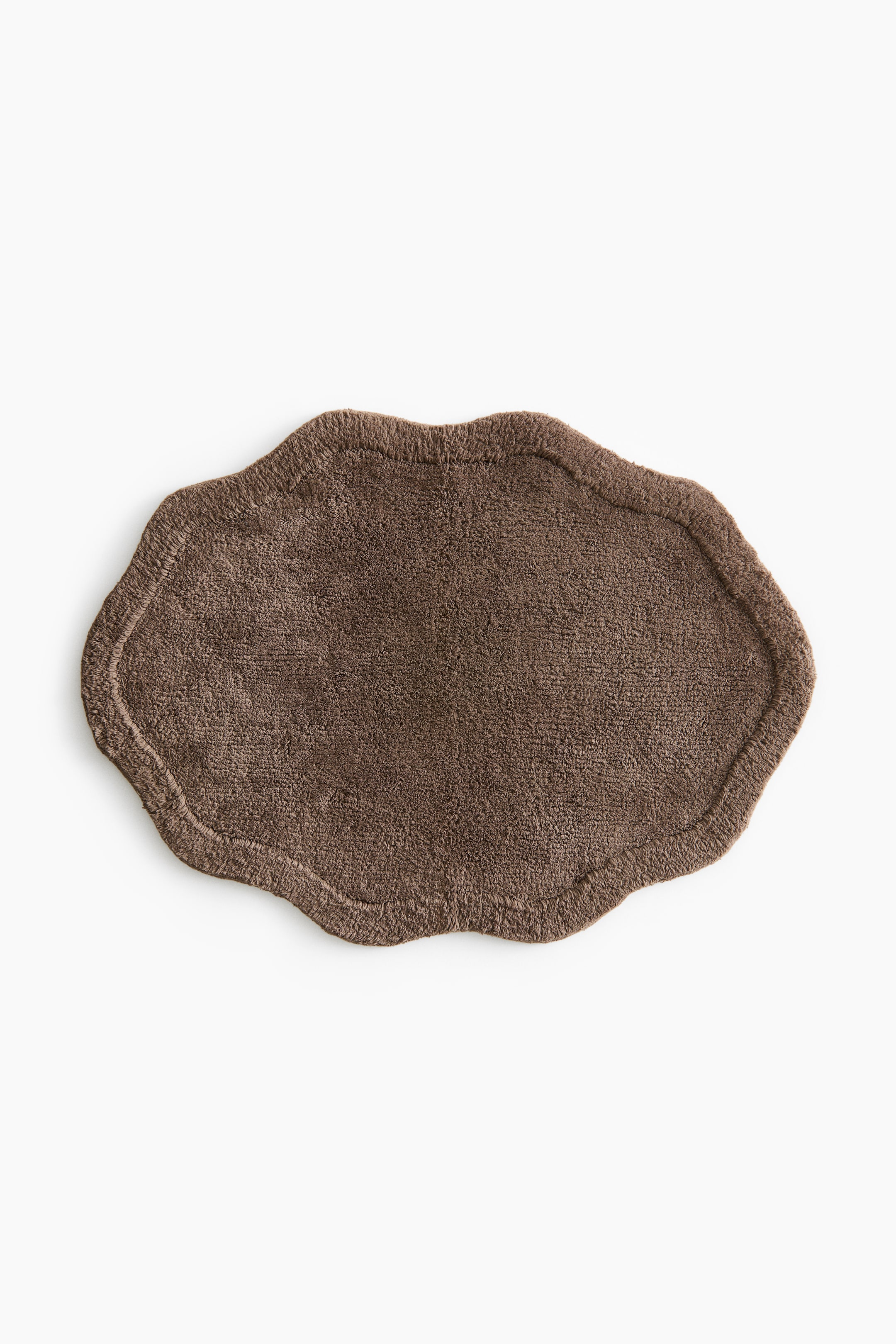 View larger image: A brown bath mat showcases a wavy, art deco-inspired silhouette, with its surface displaying a tufted cotton texture. A raised border outlines its irregular edge.