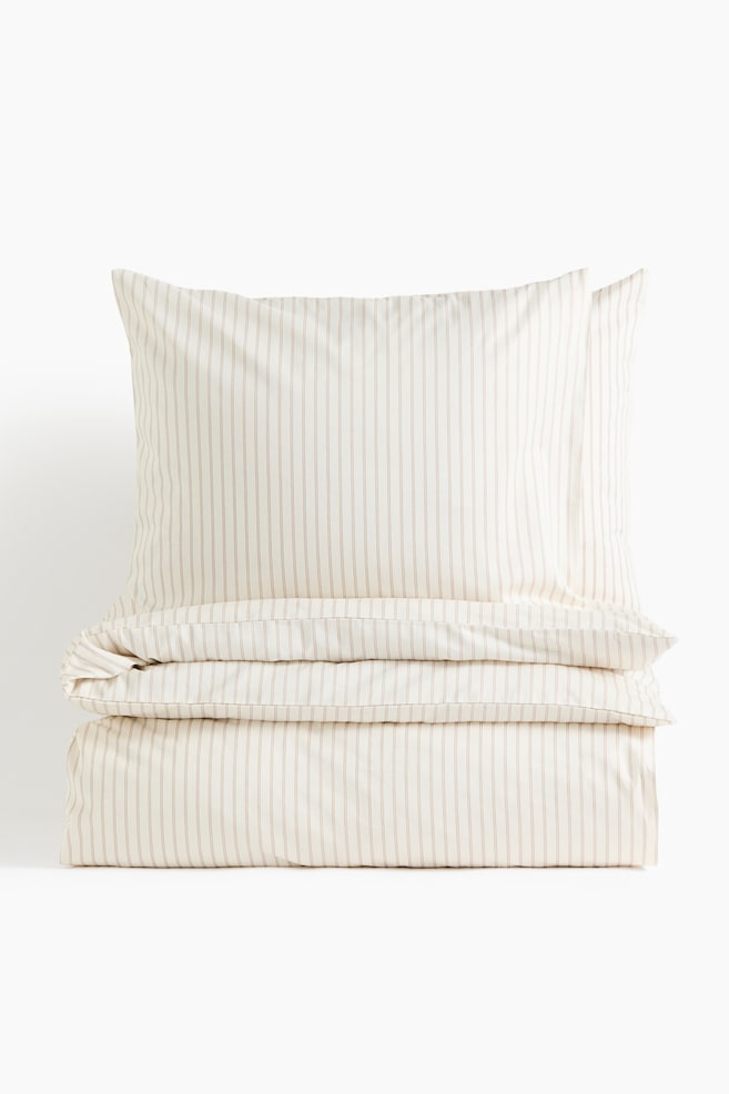 A front-facing view is showing a folded quilt cover set in off-white cotton sateen with a thin, vertical beige striped pattern. Two matching pillowcases are standing upright on top of the neatly folded quilt cover. - 1