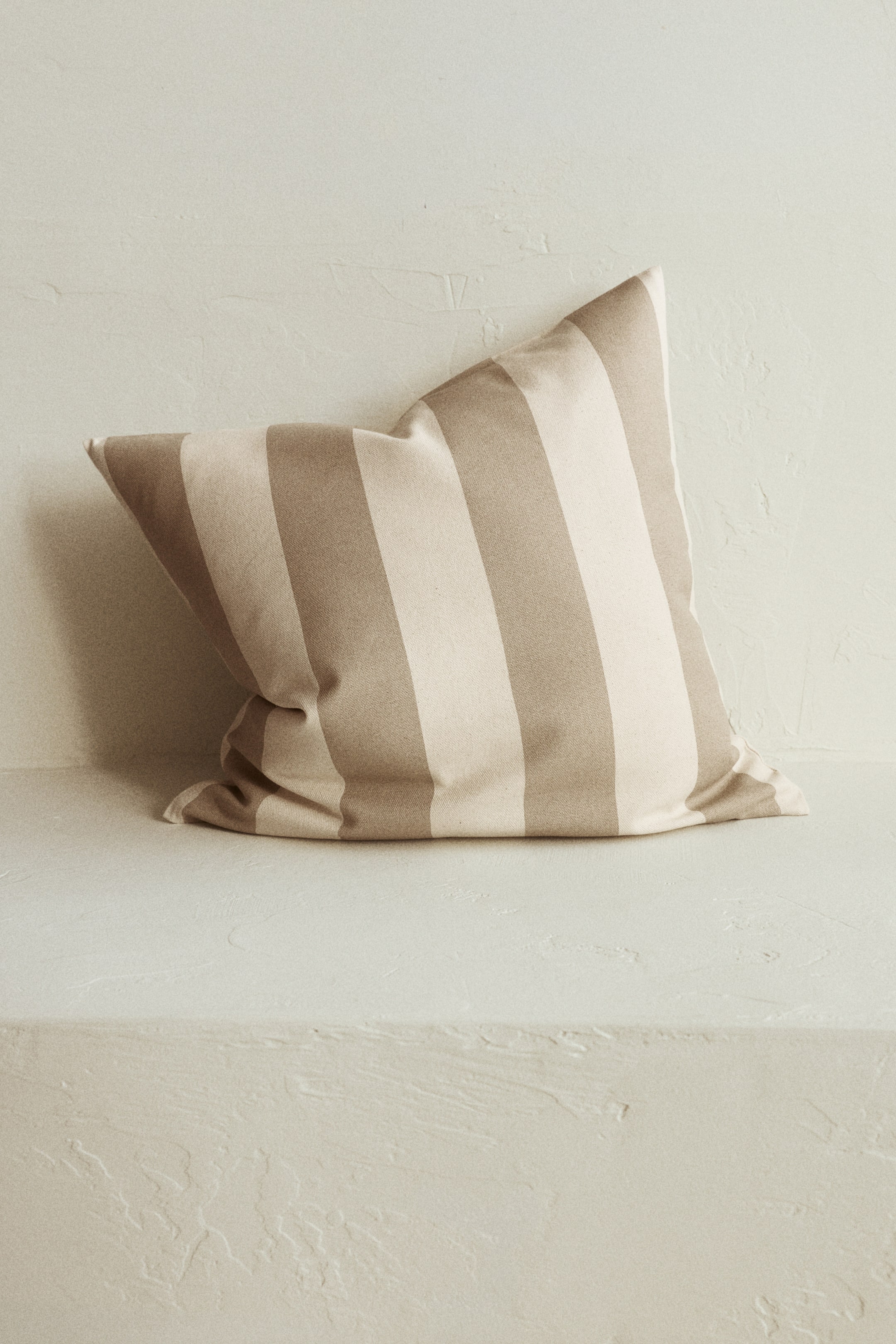拡大画像を表示: ライトベージュとタンカラーの縦ストライプが交互に施された枕は、右上の角が持ち上がっているため、下部の縁にわずかなシワが生じています。