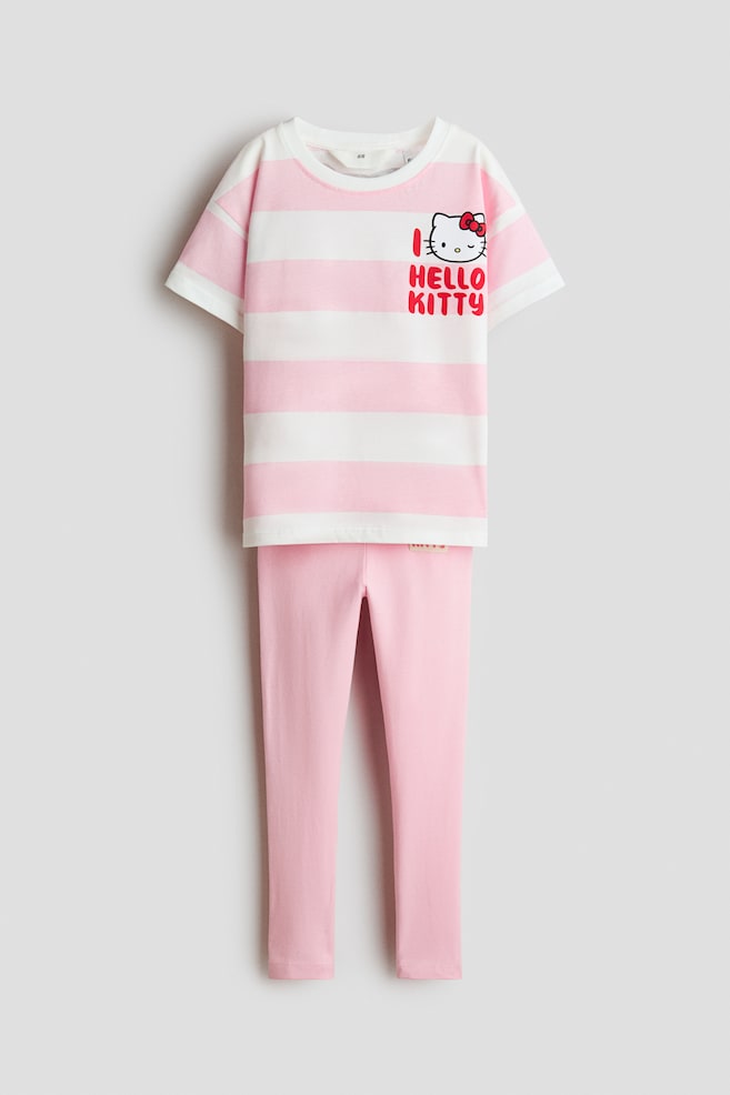 Ein zweiteiliges Baumwoll-Set ist von vorne zu sehen und besteht aus einem kurzärmeligen T-Shirt mit Rundhalsausschnitt in rosa-weiÃen Querstreifen sowie einer dazu passenden einfarbig rosa Leggings. Auf der linken oberen Brust des T-Shirts befindet sich eine Hello Kitty-Grafik mit dem roten Schriftzug âI HELLO KITTYâ. - 1