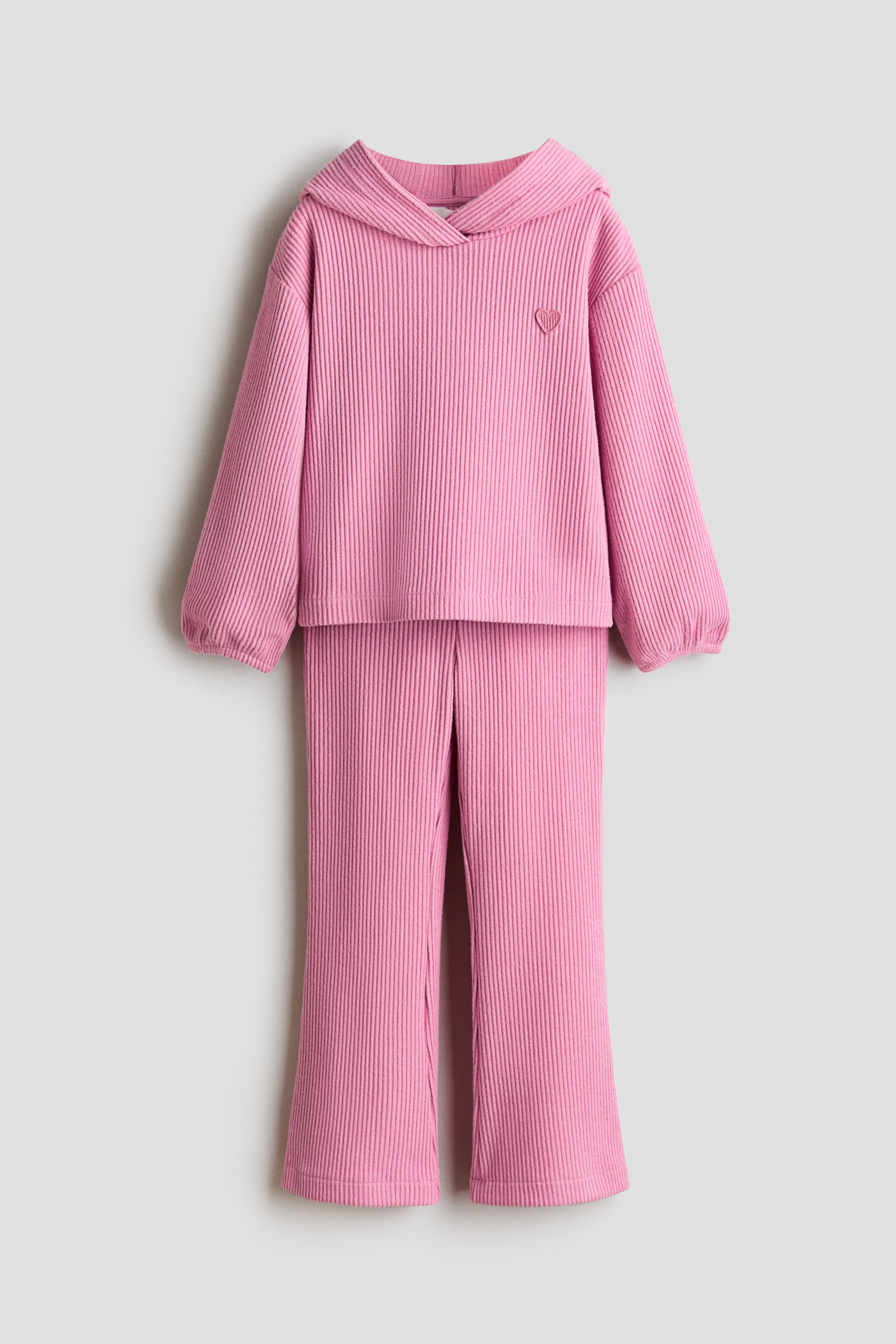 View larger image: A pink ribbed two-piece set is showcasing a front-facing view, highlighting a long-sleeved hoodie with a hood, elasticized cuffs, and an embroidered heart on the left chest, paired with matching flared pants.