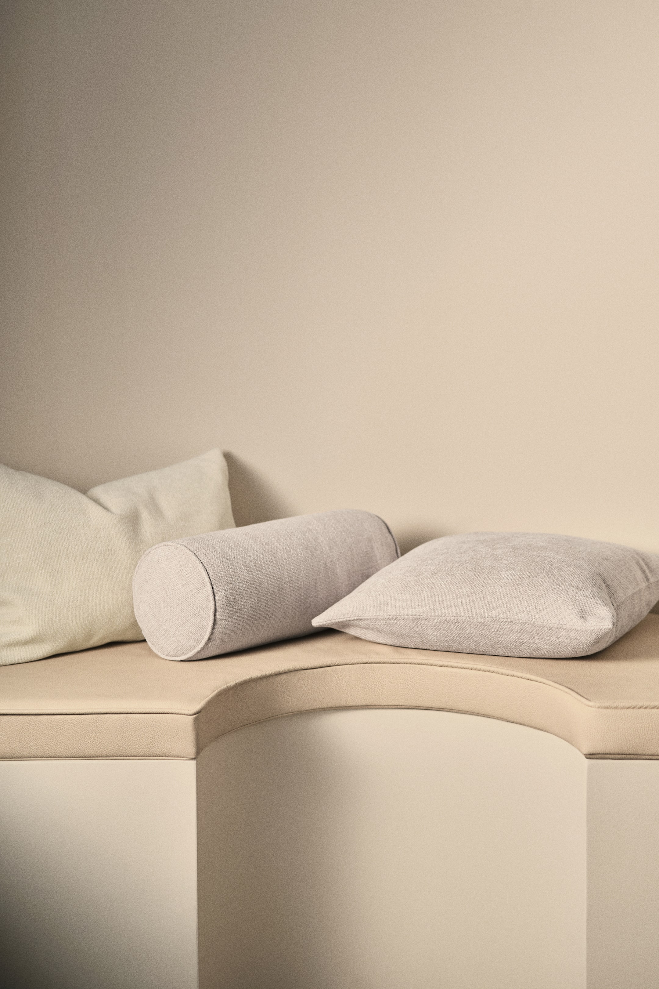 Grotere afbeelding bekijken: Een bolster wordt gepresenteerd in een licht beige, zachte chenille weefsel, met biezen rond de cirkelvormige uiteinden.