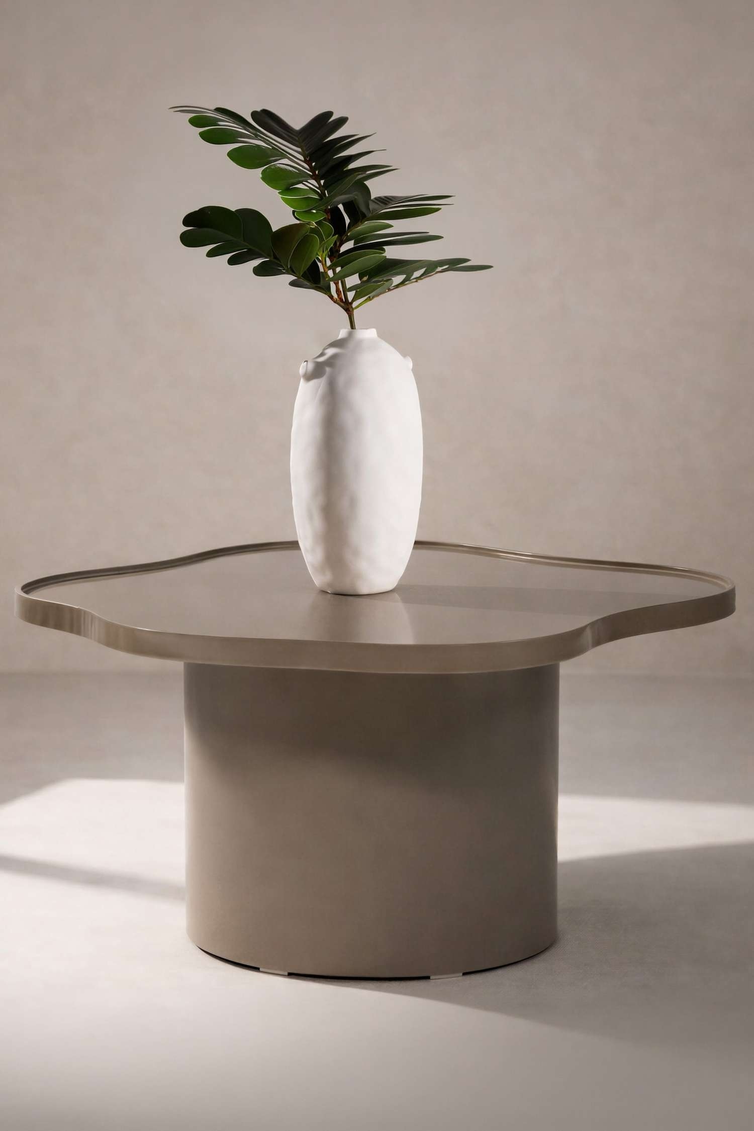Et olivenbrunt sofabord med en organisk formet top og en diskret forhøjet kant, der hviler på en cylindrisk piedestalbase, vist fra en let forhøjet front-højre vinkel.